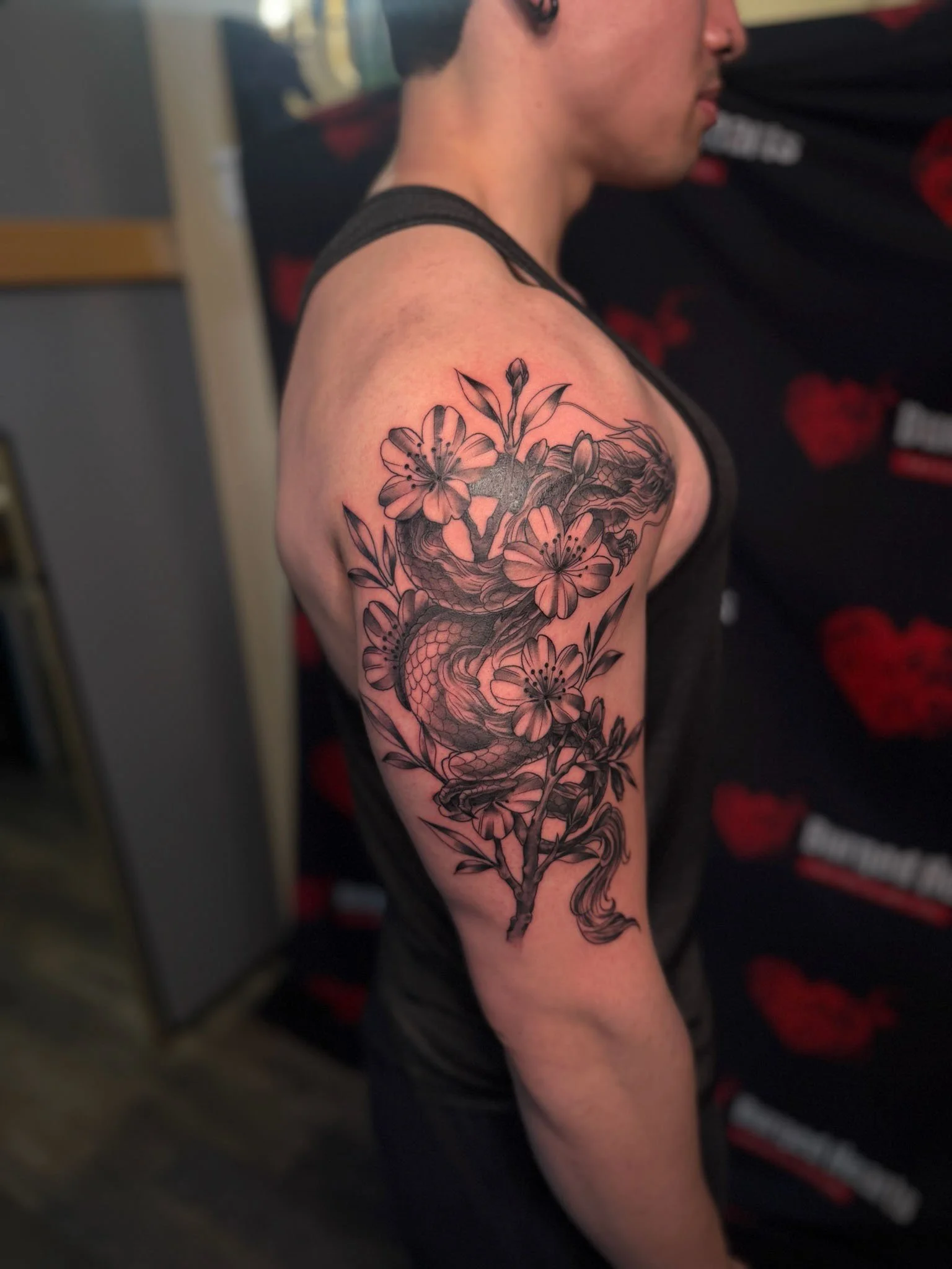 A person's upper arm tattoo depicting a snake intertwined with cherry blossoms.