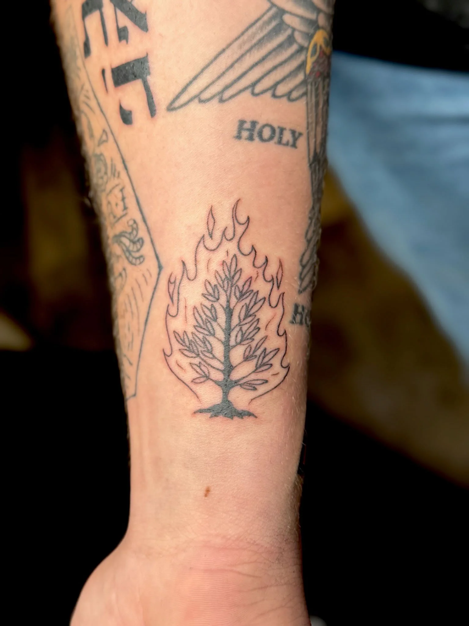 Tattoo of a burning tree with flames surrounding it, located on a person's forearm.