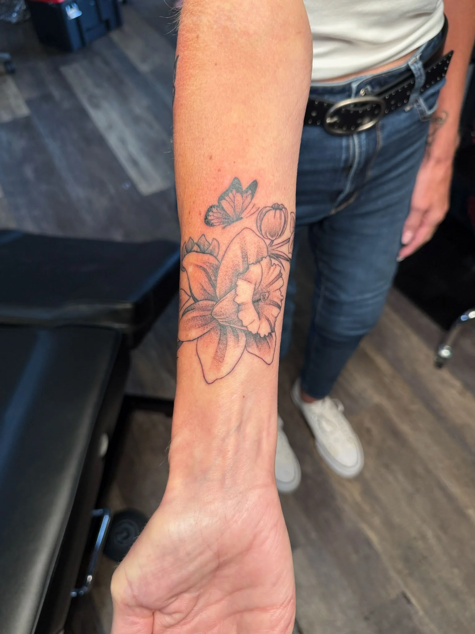 Tattoo of a butterfly, tulip, and daffodil flowers on a person's forearm.