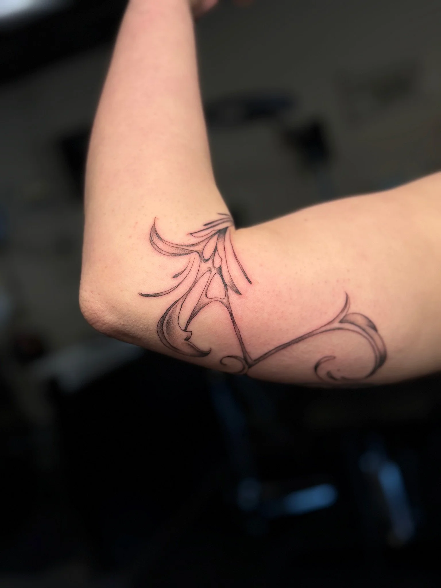 A tattoo of an ornate design with flowing lines on the inside of a person's upper arm.