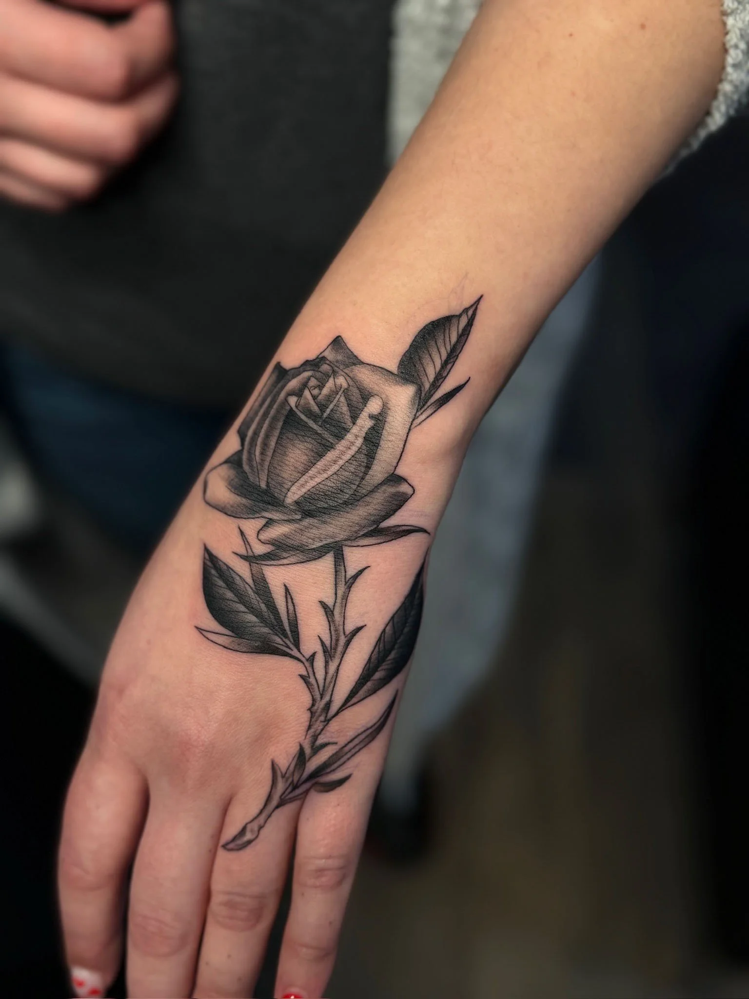 Black and gray tattoo of a rose with leaves on a person's forearm.