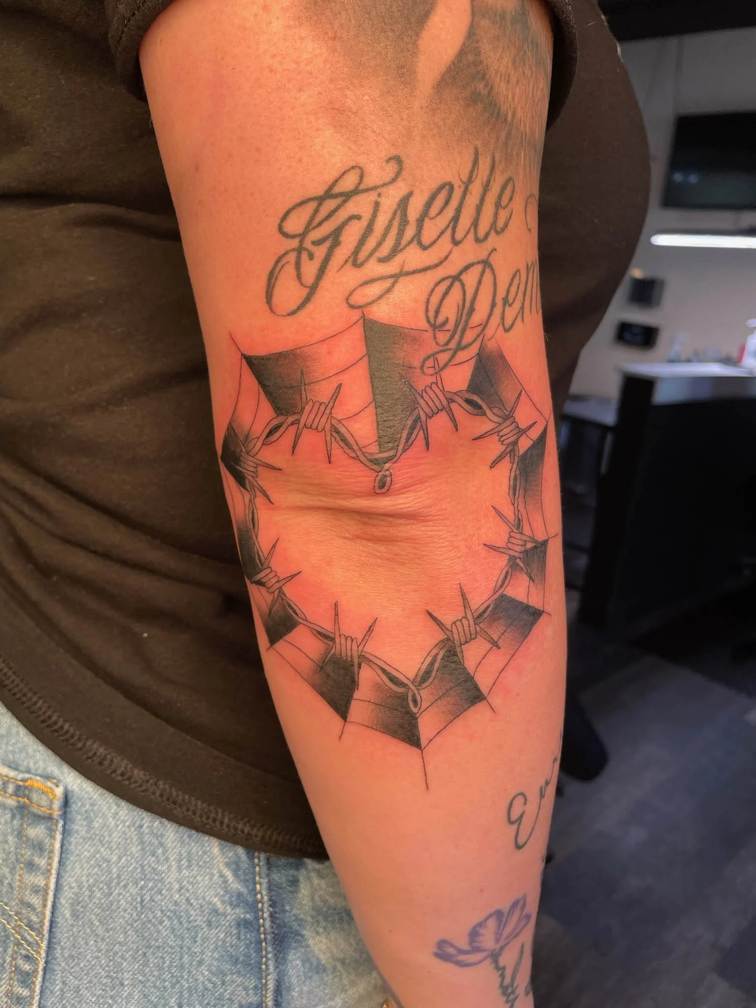 Tattoo of a heart with barbed wire and a phrase above it, on a person's arm.