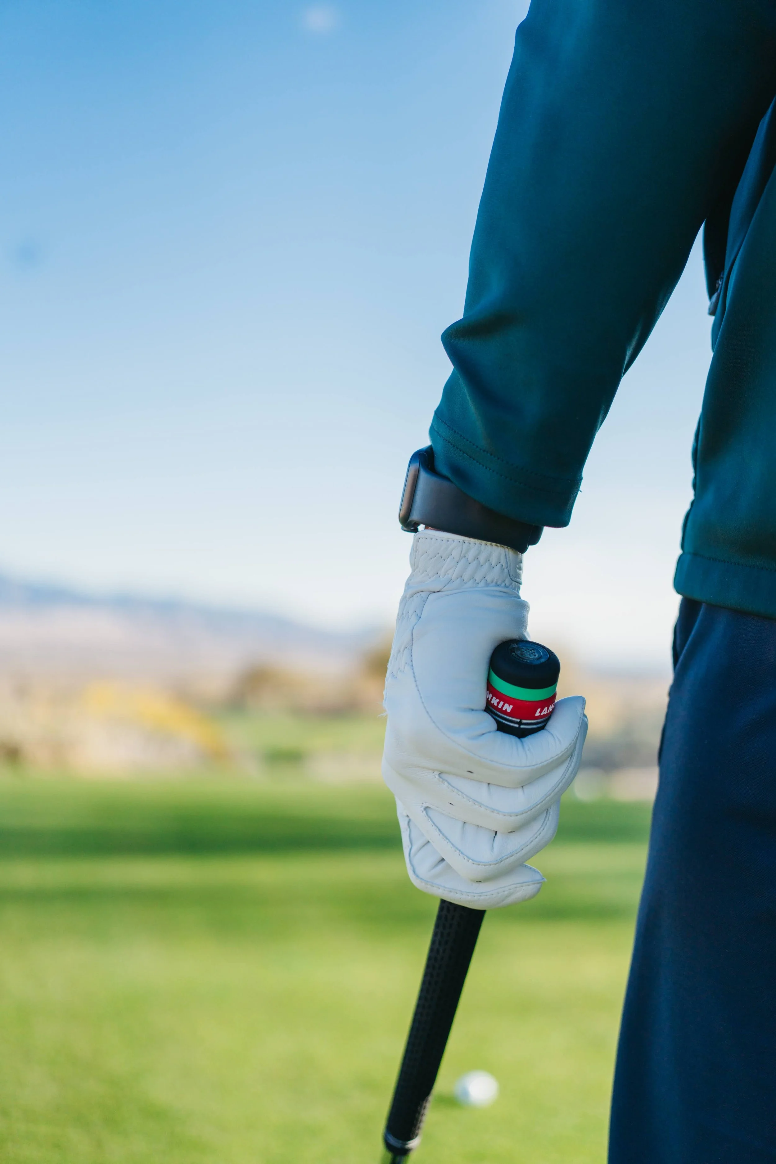 Close-up of a person wearing a golf glove and holding a golf club on a golf course.