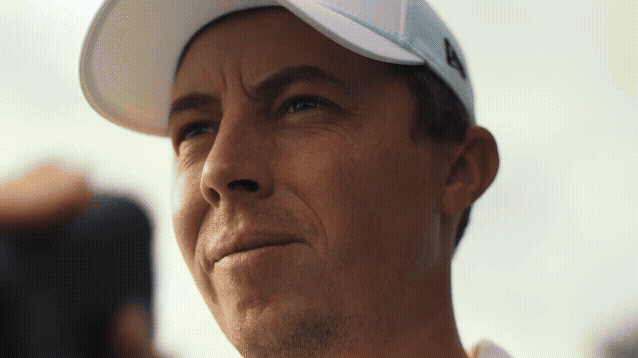 Close-up of a man wearing a white baseball cap, looking serious and slightly squinting.