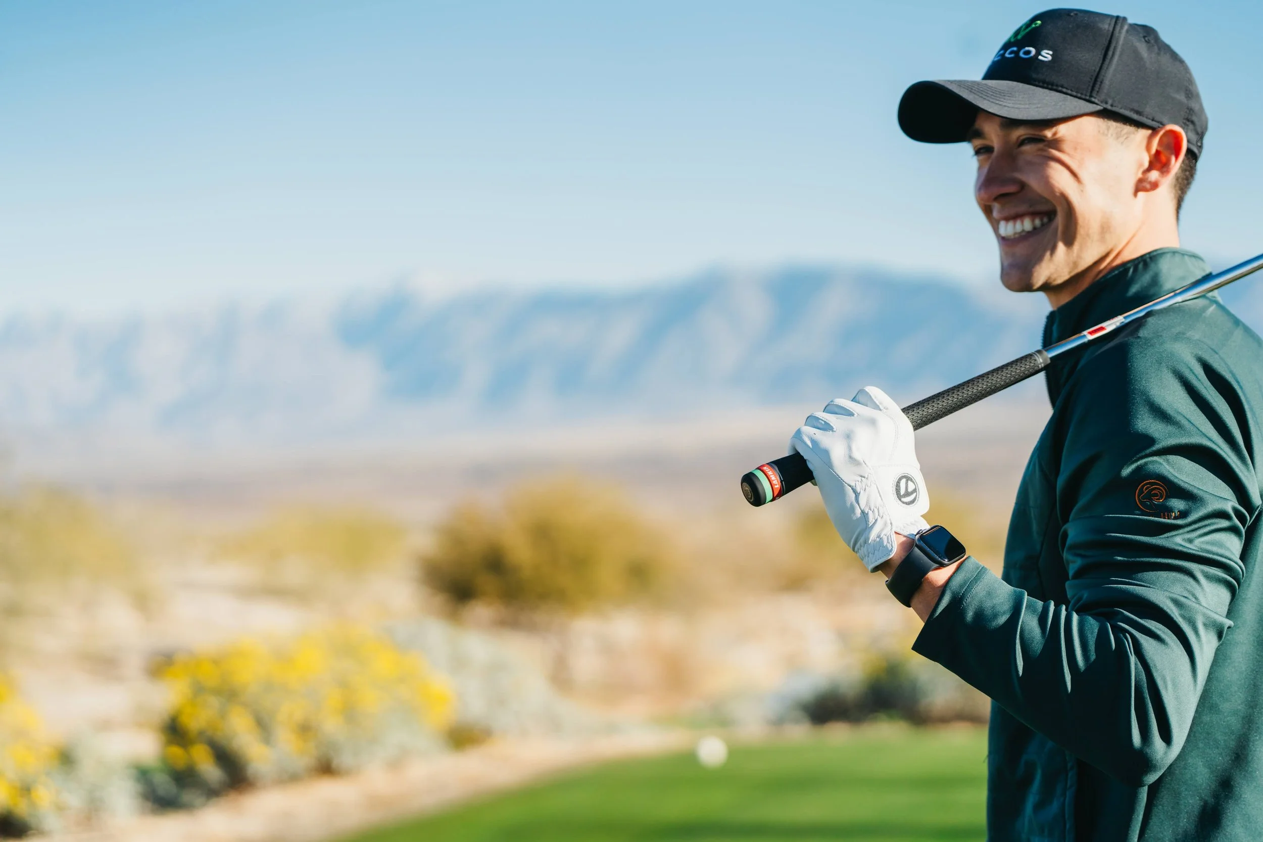 Happy man holding a golf club on a golf course with mountains in the background.