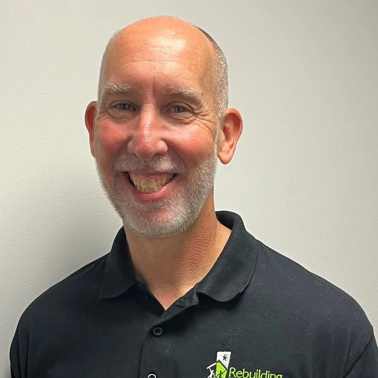 A middle-aged bald man, smiling. He's in a black shirt against a plain background.
