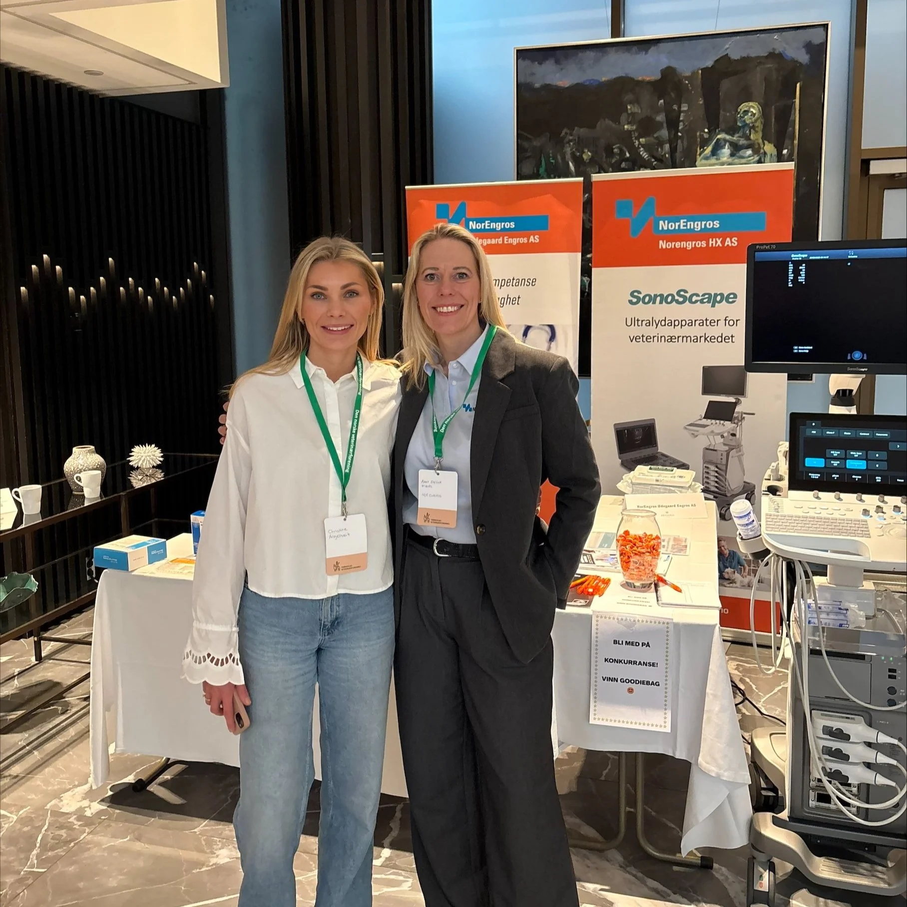 To kvinner står sammen foran en utstillingsstand med banners fra NorEngros og SonoScape, på et konferansesenter.