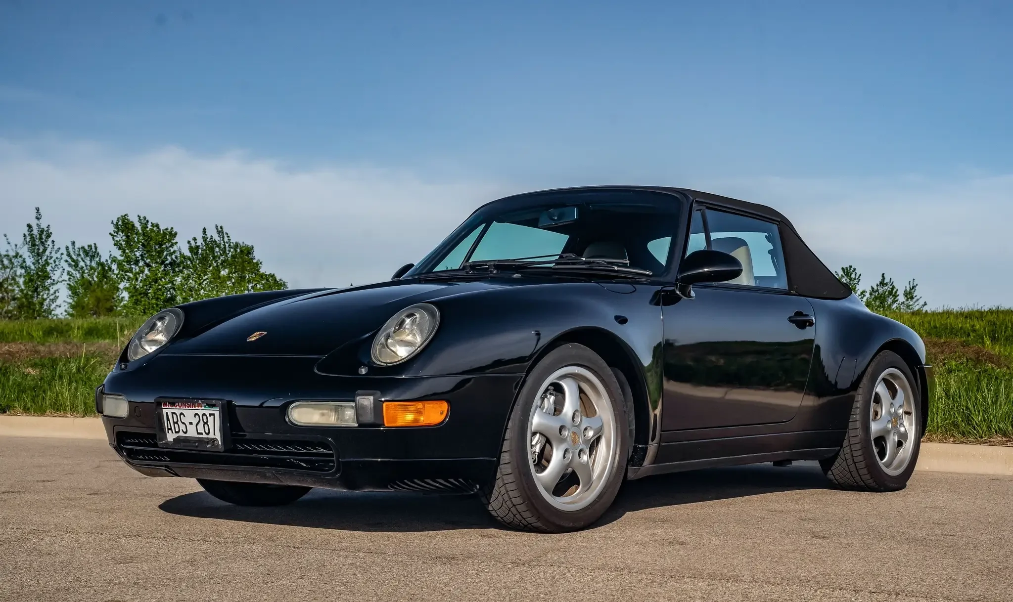 a gorgeous black 1995 Porsche 993 convertible, parked outside with a clear blue sky in the background
