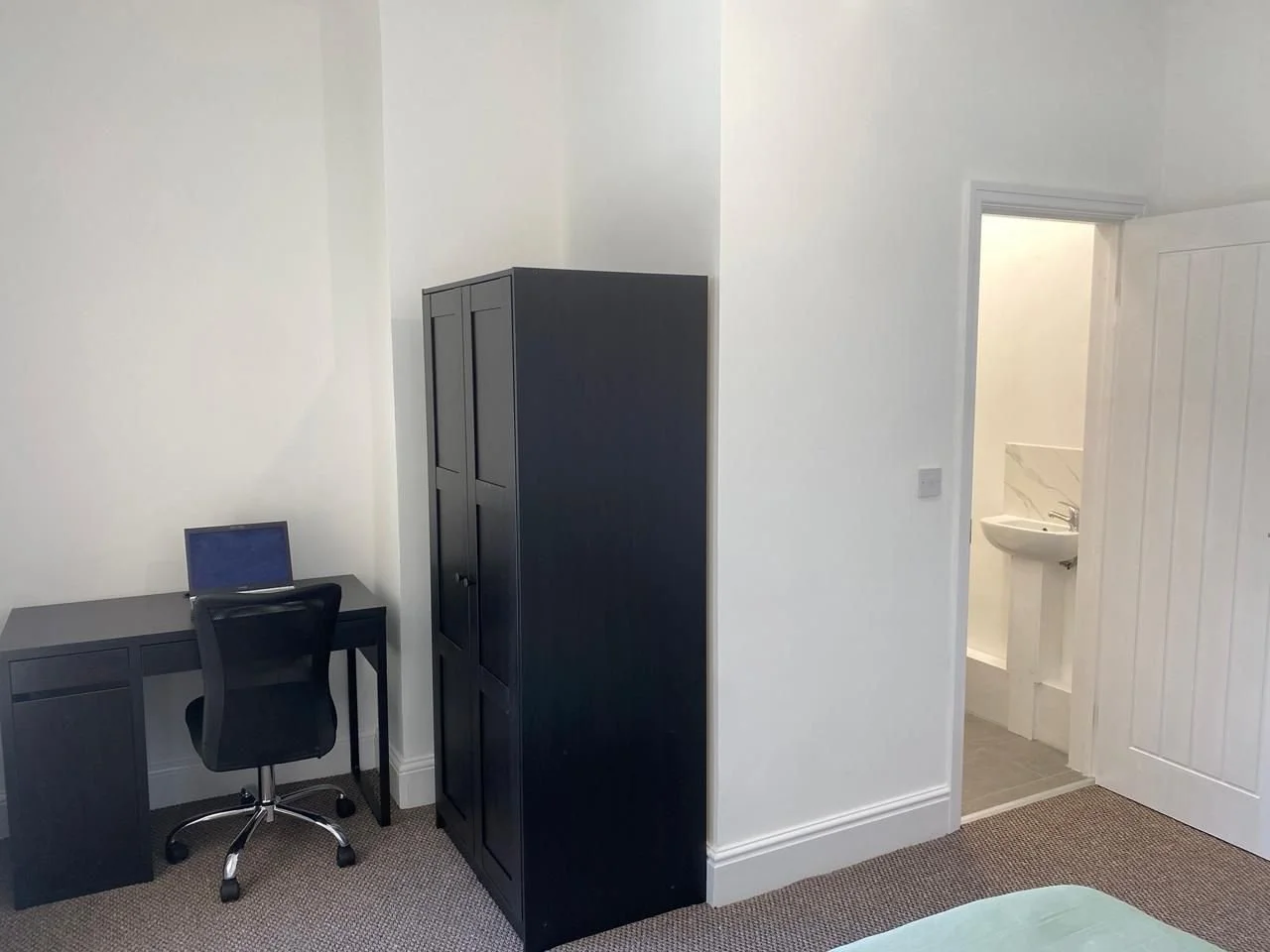 Room with black desk and chair, black cabinet, and a door leading to a bathroom with a sink visible.