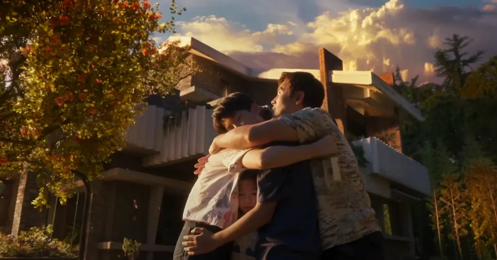 A family hugging in front of a large home with a tree next to them with golden fall foliage