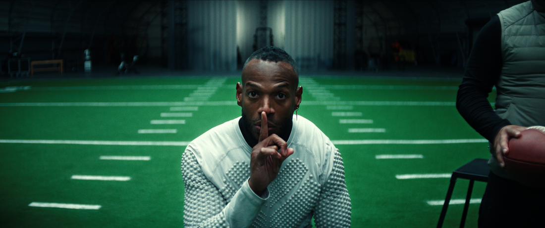 Marlon Wayans in the film HIM. He's in a training compound and has a finger over his mouth as though he's trying to silence someone