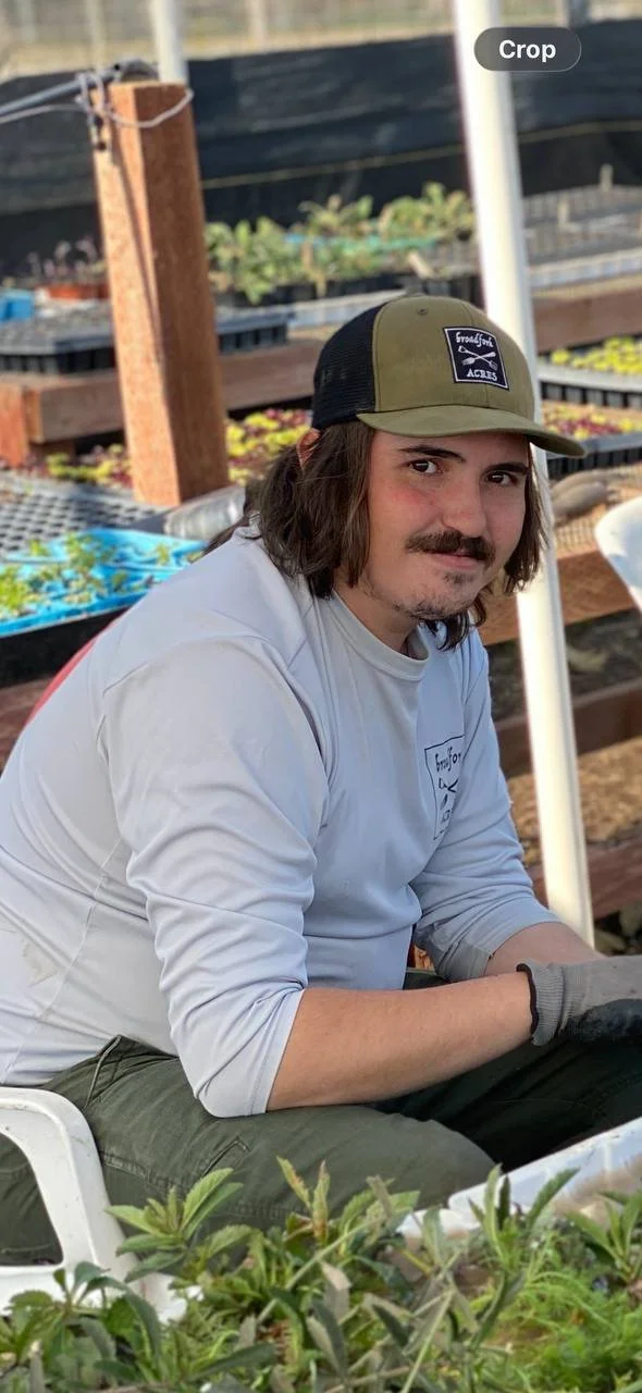 Young man with long hair smiling while propagating nursery plants at a small farm in Bakersfield.