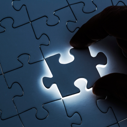 A hand places the final puzzle piece into a glowing puzzle, symbolizing completion or problem-solving.