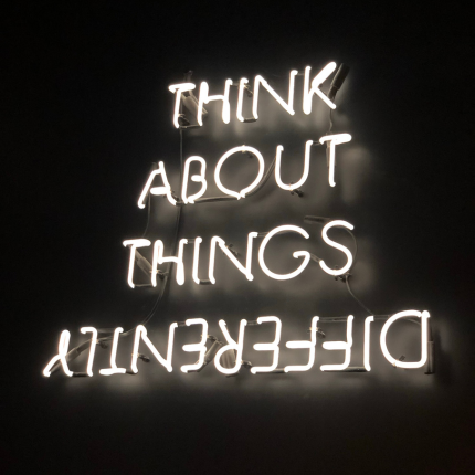 A neon sign reads “Think About Things Differently,” with the words flipped upside down.