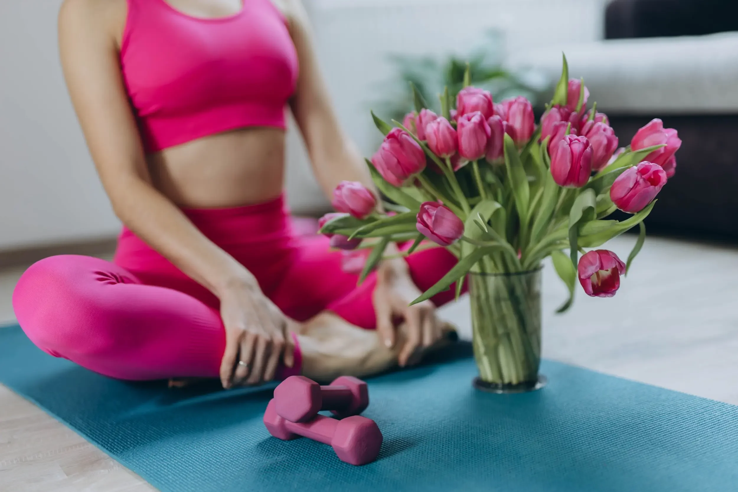 A woman wearing pink workout clothes with a vase of tulips.