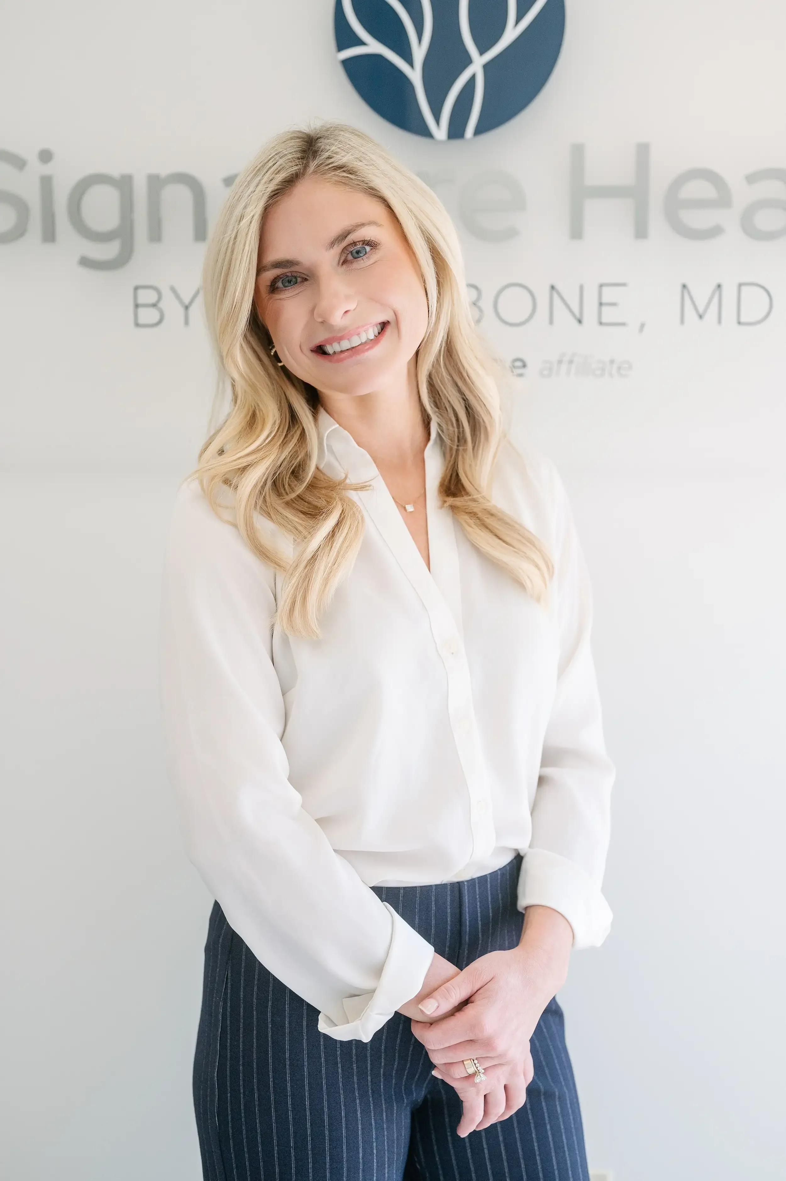 Maggie Theriot, DNP, FNP-C, nurse practitioner at Signature Health by Robin Bone, MD, standing at the practice logo wall in Metairie, LA