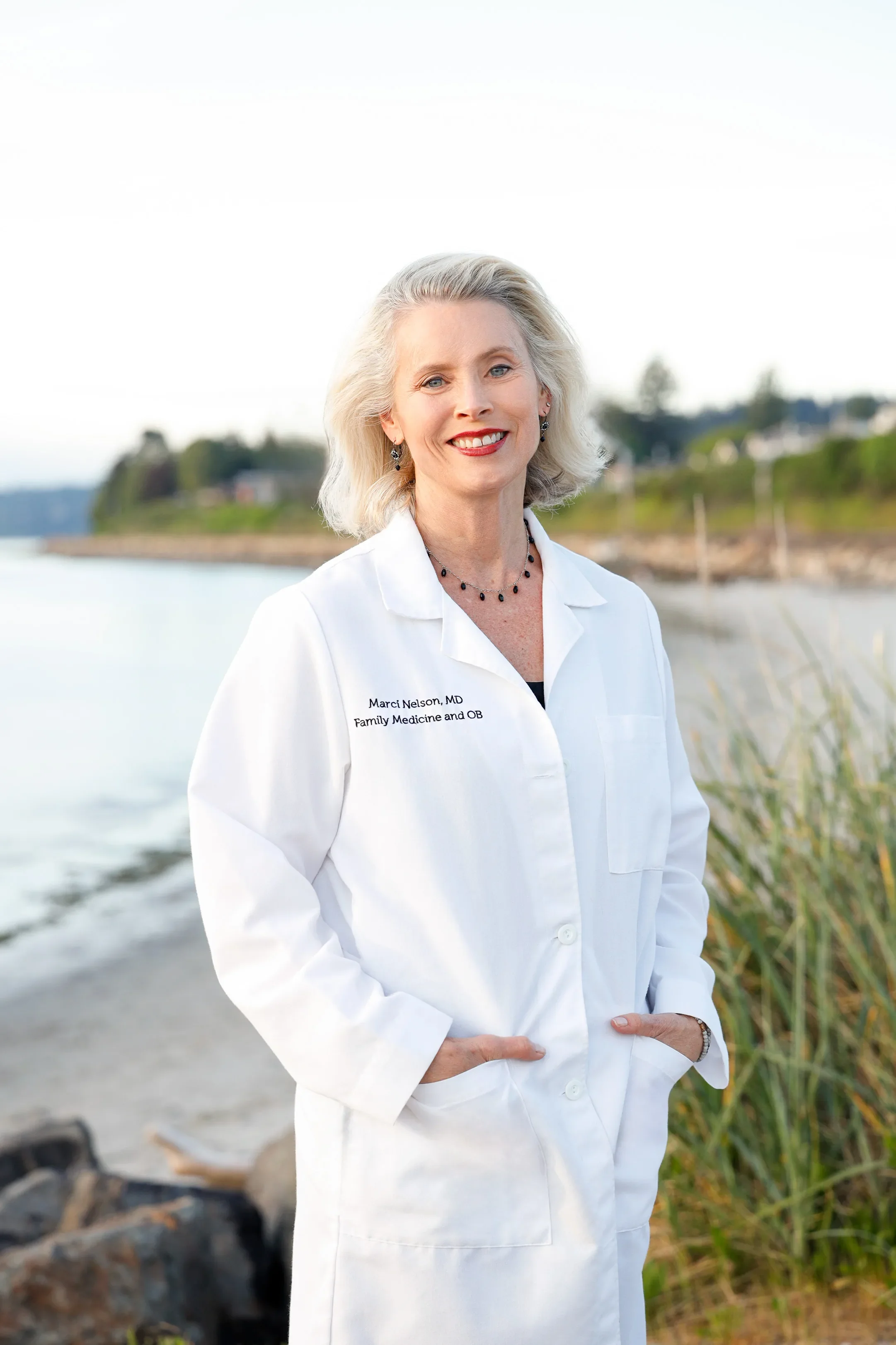 Dr. Marci Nelson, MD, MSCP, concierge family medicine physician at Trillium Concierge Medicine, standing outdoors along the Puget Sound shoreline in Shoreline, WA