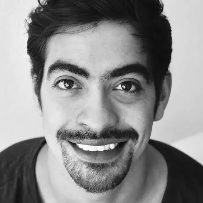 Schwarz-weiß Porträt eines lächelnden Mannes mit Bart und dunklem Haar.