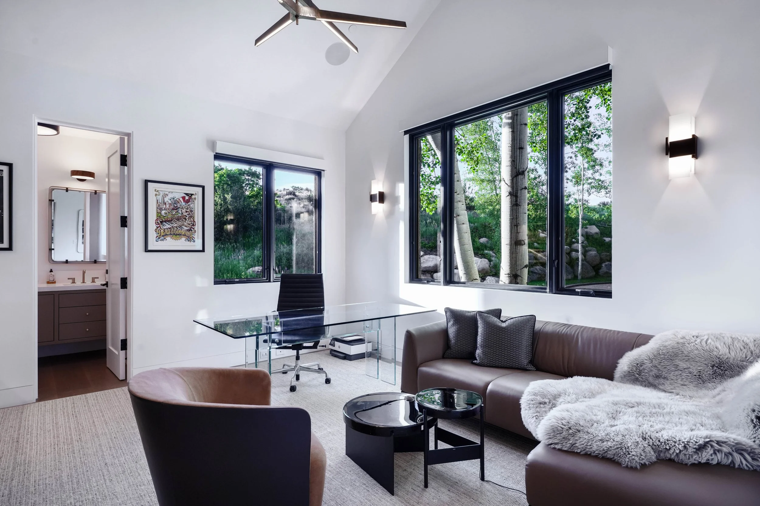 Modern home office with leather seating, glass desk, vaulted ceiling, and floor-to-ceiling windows overlooking aspen trees — Colorado luxury home photography by Refine Imagery