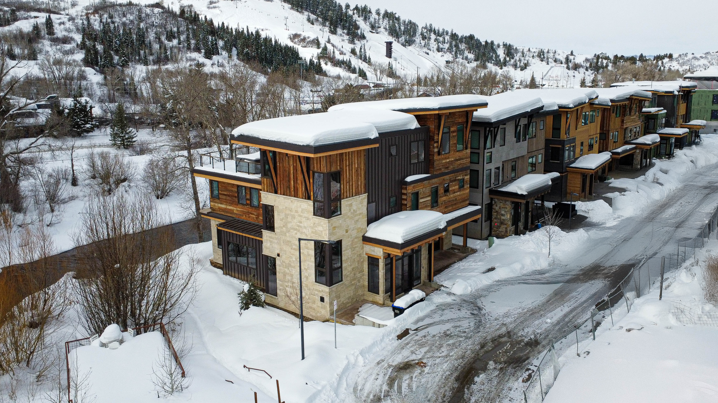 Aerial drone photograph of contemporary mountain townhomes with stone and timber facade in winter snow with ski slope views — real estate drone photography by Refine Imagery