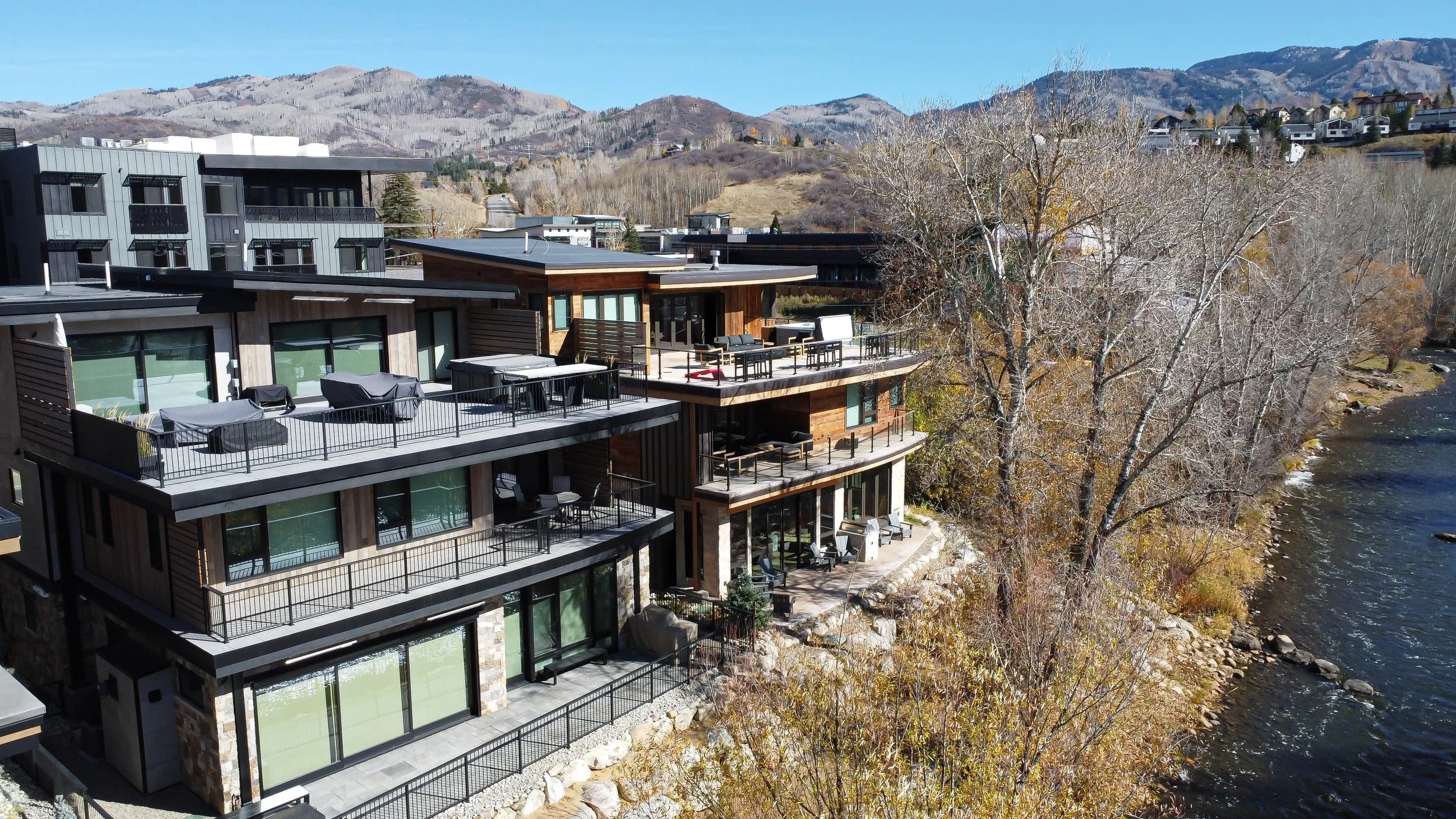 Drone aerial photo of modern multi-level riverfront luxury property with rooftop terraces and mountain backdrop in Colorado — Refine Imagery real estate drone photography
