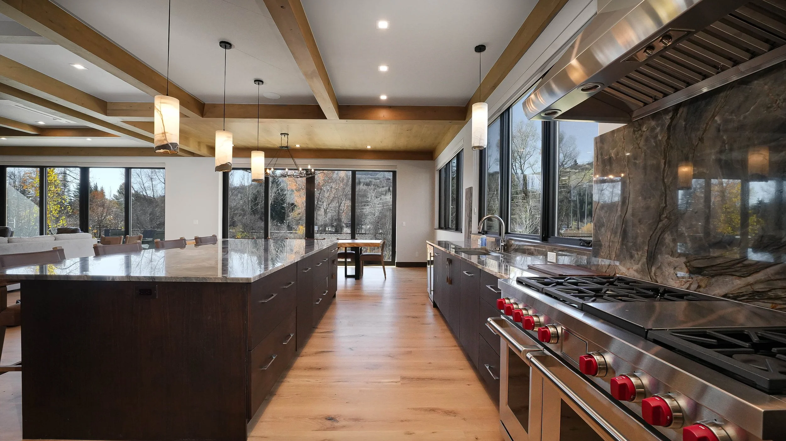 Professional chef's kitchen with commercial-grade Wolf range, stone slab backsplash, dark cabinetry, and exposed timber beam ceiling — luxury real estate photography by Refine Imagery