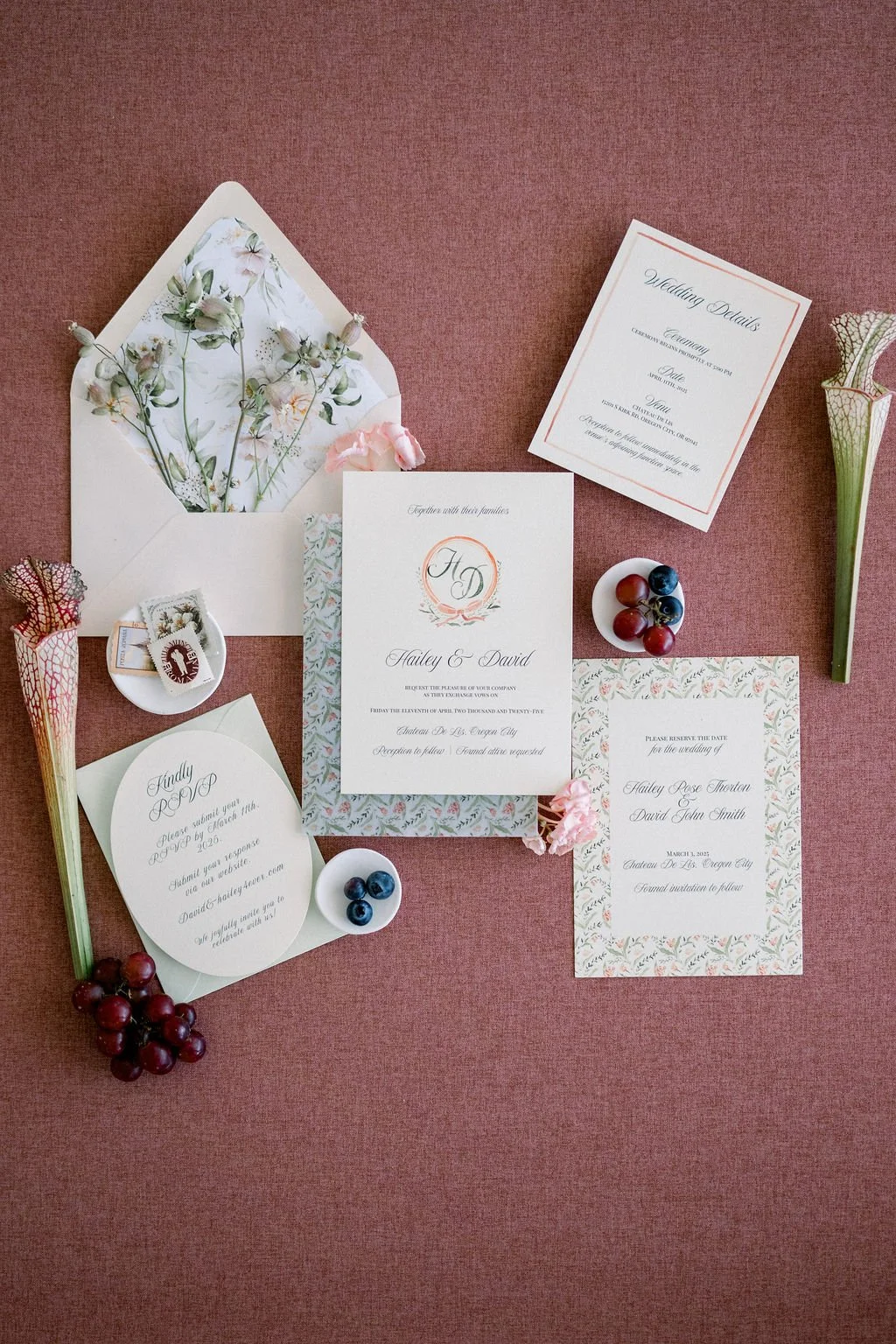 Wedding invitation suite with floral accents, berries, and an envelope with pressed flowers on a pink background.