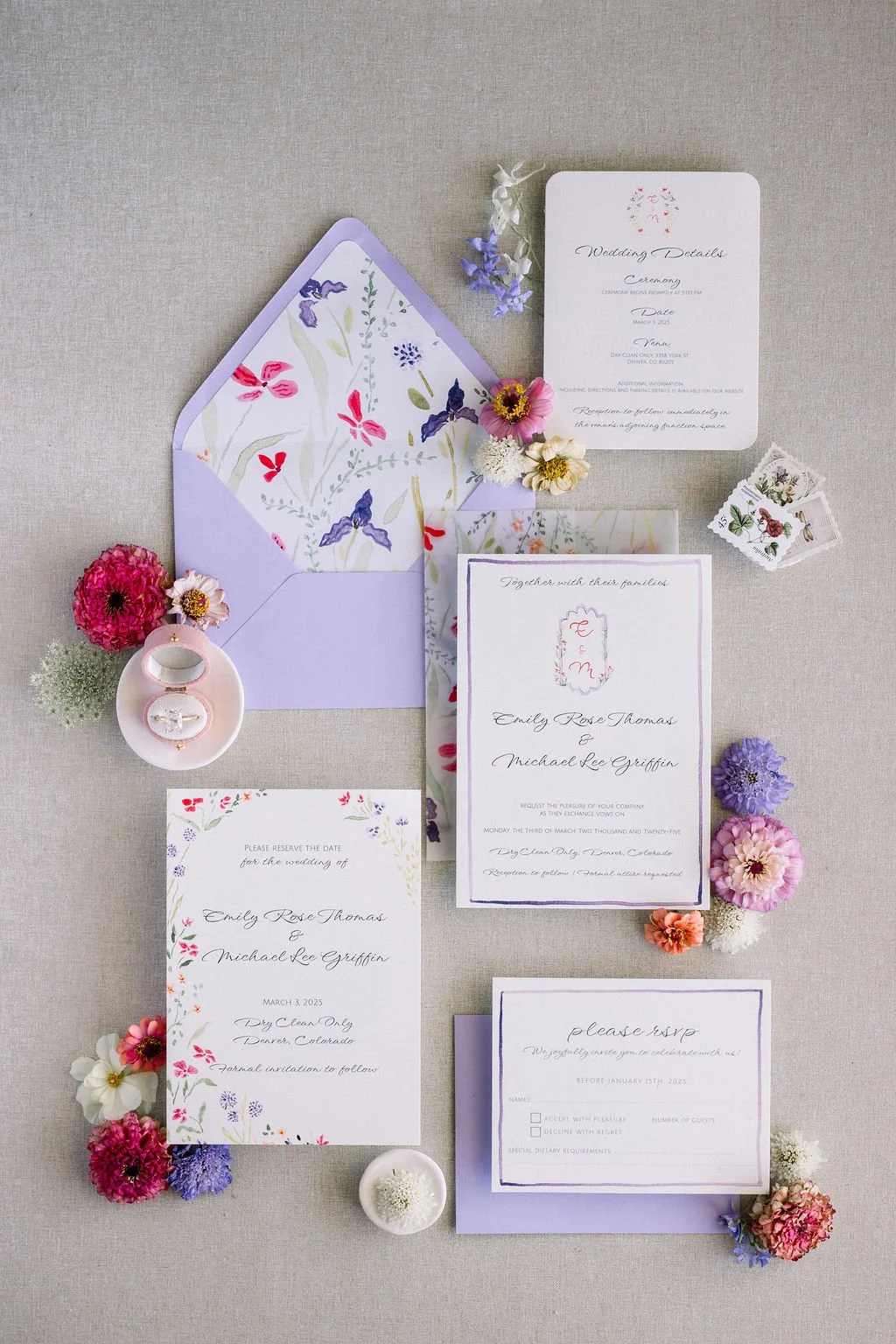 Wedding invitation suite with floral accents, including RSVP card, wedding details card, and envelope decorated with colorful flowers and wedding rings.