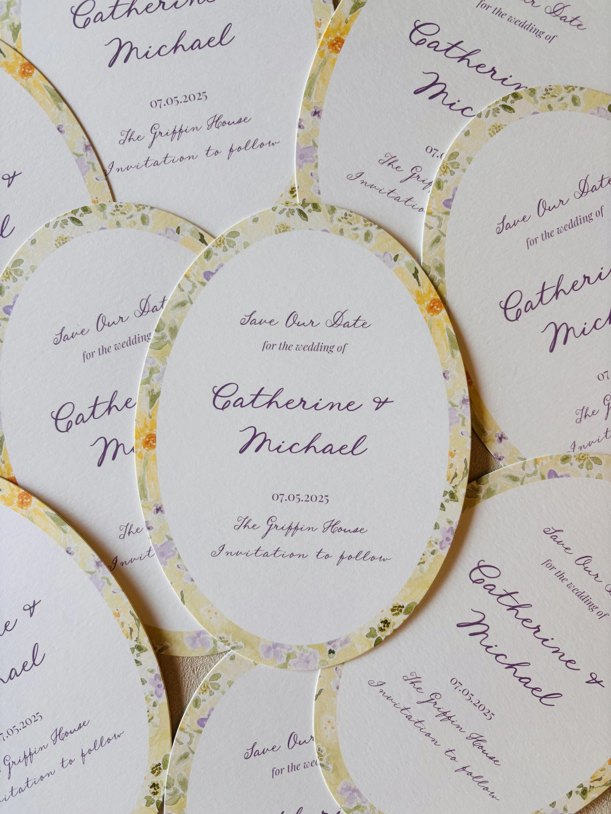 Multiple wedding invitations with floral borders, featuring purple cursive text for the names Catherine and Michael, and details of the wedding date, location, and invitation to follow.