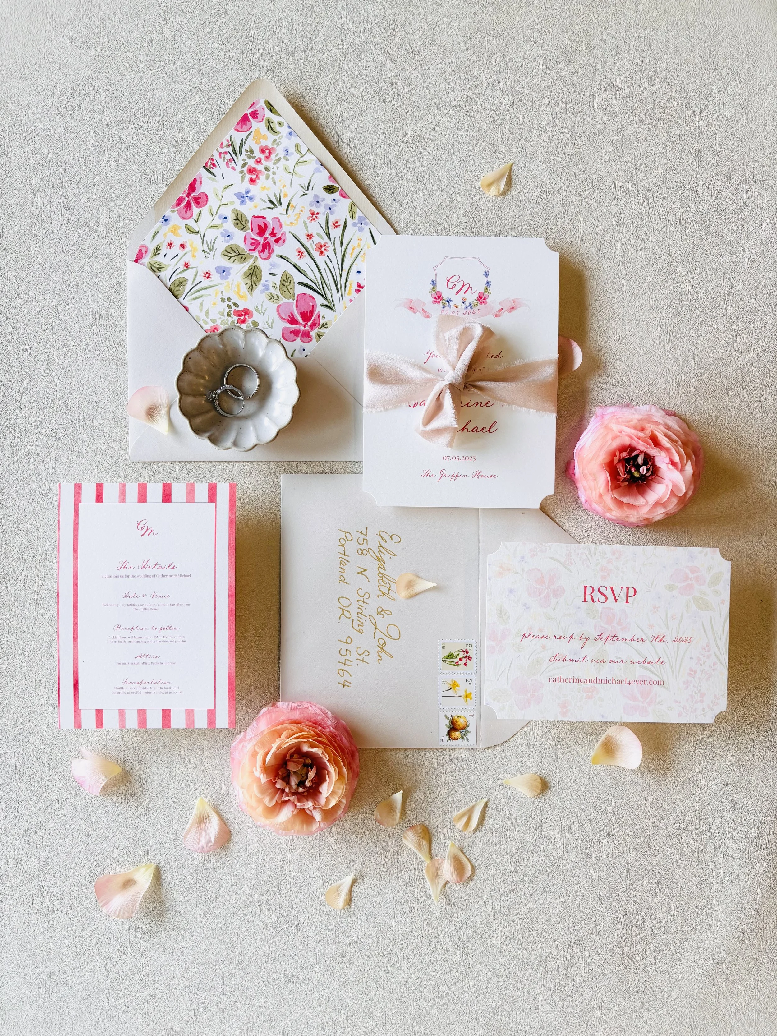 Wedding invitation set with pink and white floral accents, RSVP card, and wedding details card, decorated with pink roses and scattered flower petals.