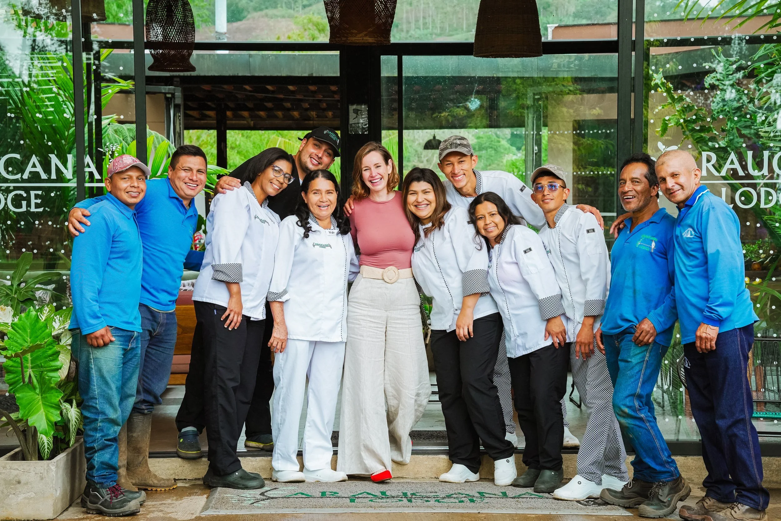 El equipo de Araucana Lodge reunido frente a la entrada de vidrio, entre plantas tropicales.