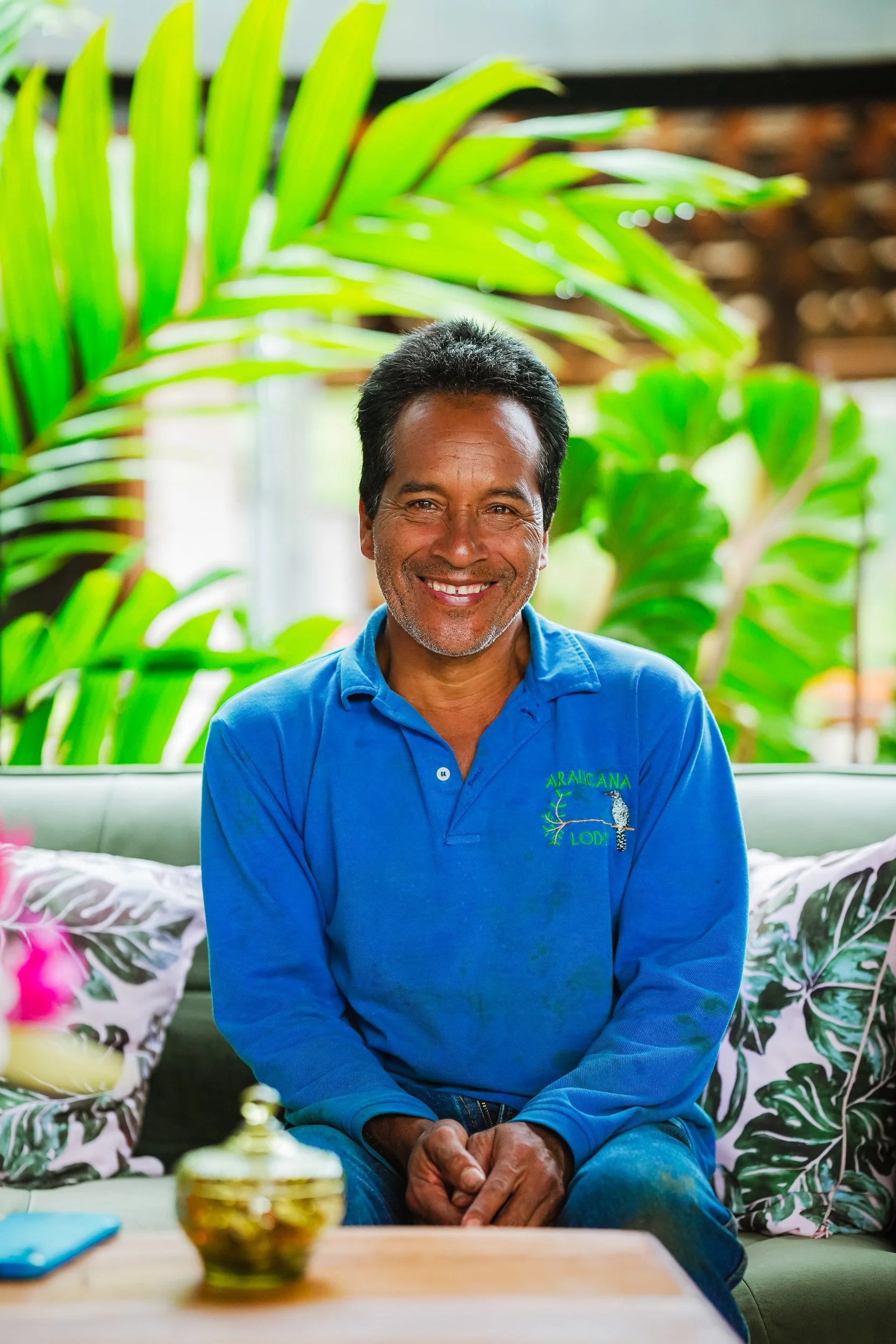 Un integrante del equipo de Araucana sonríe, sentado junto a plantas tropicales y con una camisa azul del lodge.