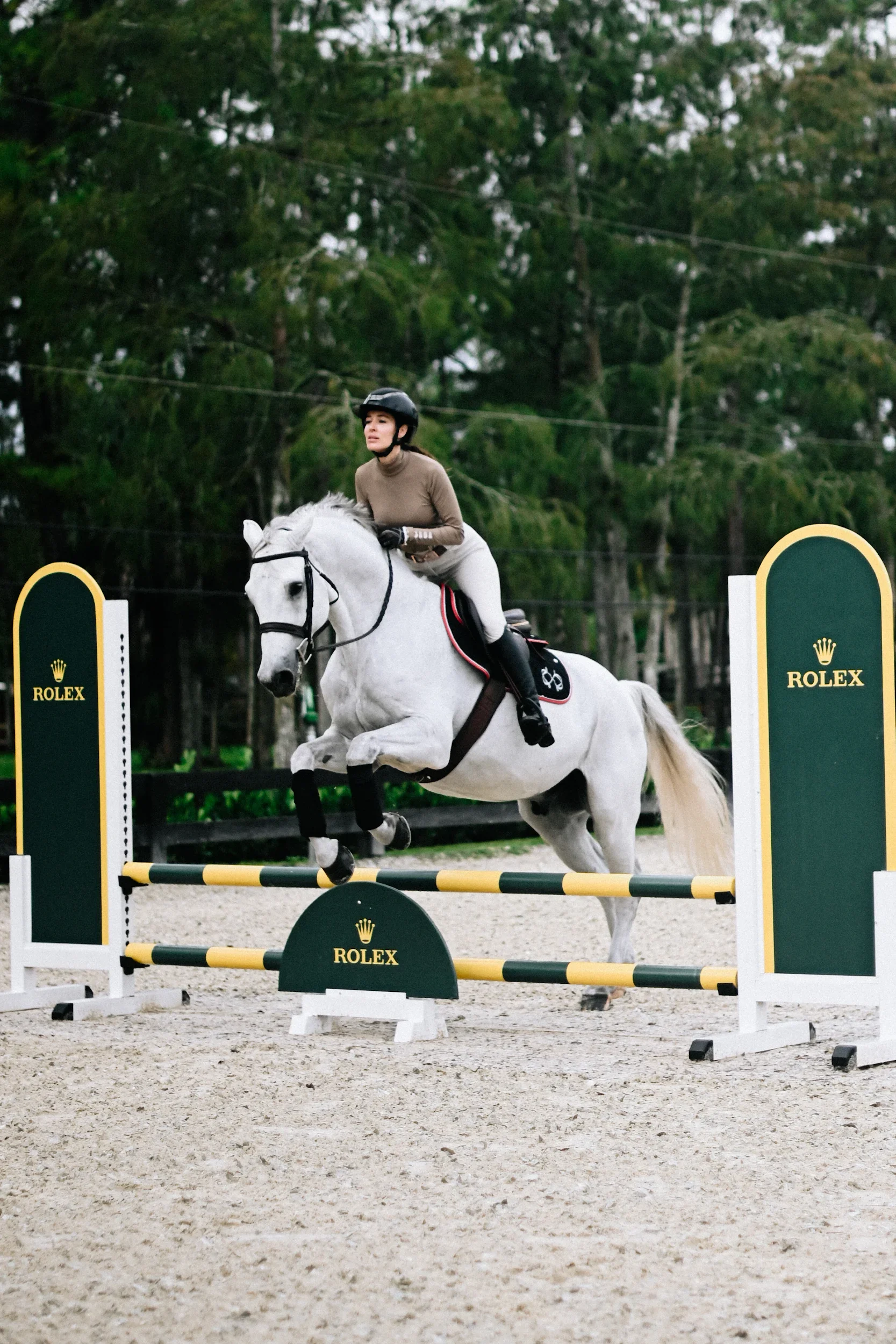 A woman riding a white horse jumps over a hurdle with "Rolex" branding during an equestrian event.