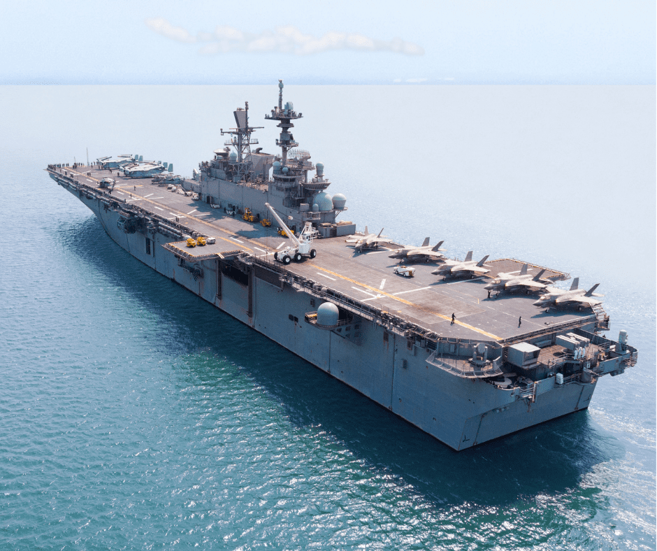 A large military aircraft carrier sailing in the ocean with several fighter jets on its deck and crew members walking around.