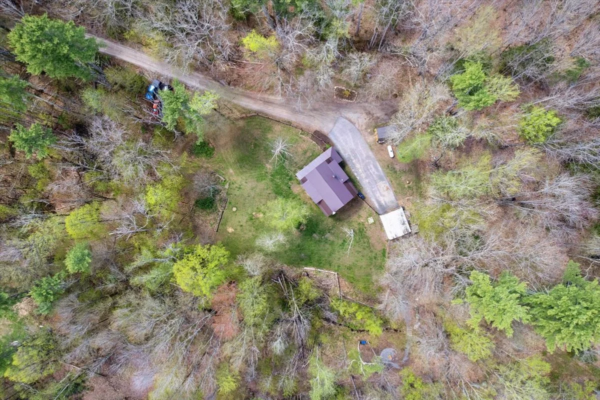 Aerial view of a house surrounded by trees and a dirt driveway leading to the house, with a small shed nearby.