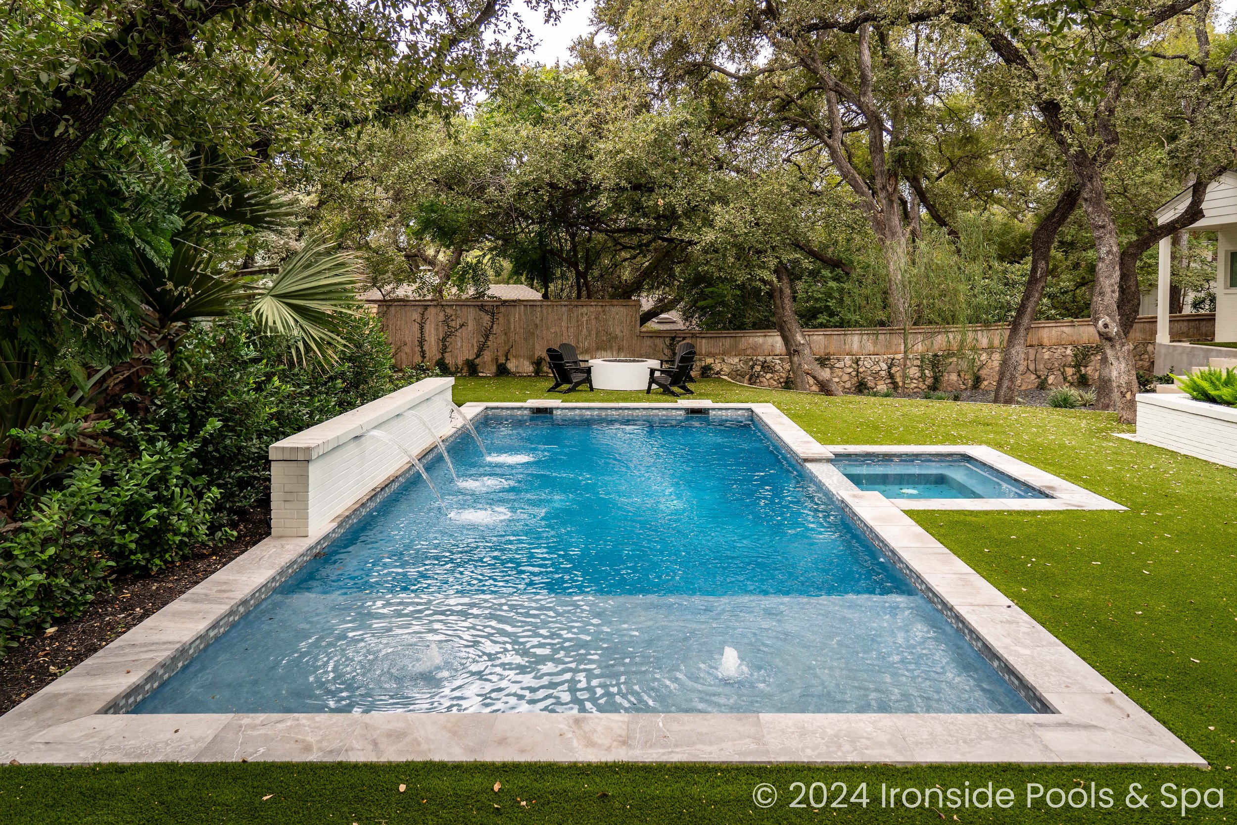 Backyard with modern swimming pool, adjacent hot tub, and patio area surrounded by trees and greenery.