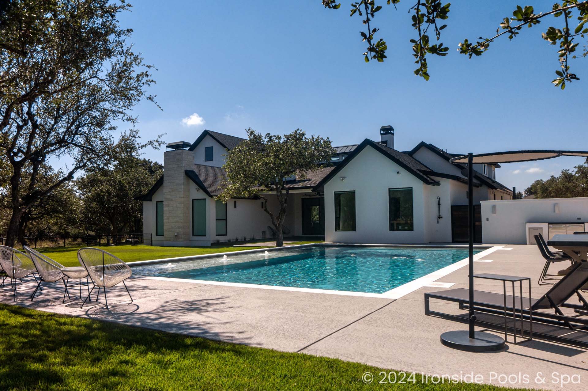 Modern house with a swimming pool in the backyard, surrounded by a lawn and trees, featuring outdoor furniture and a shaded seating area.