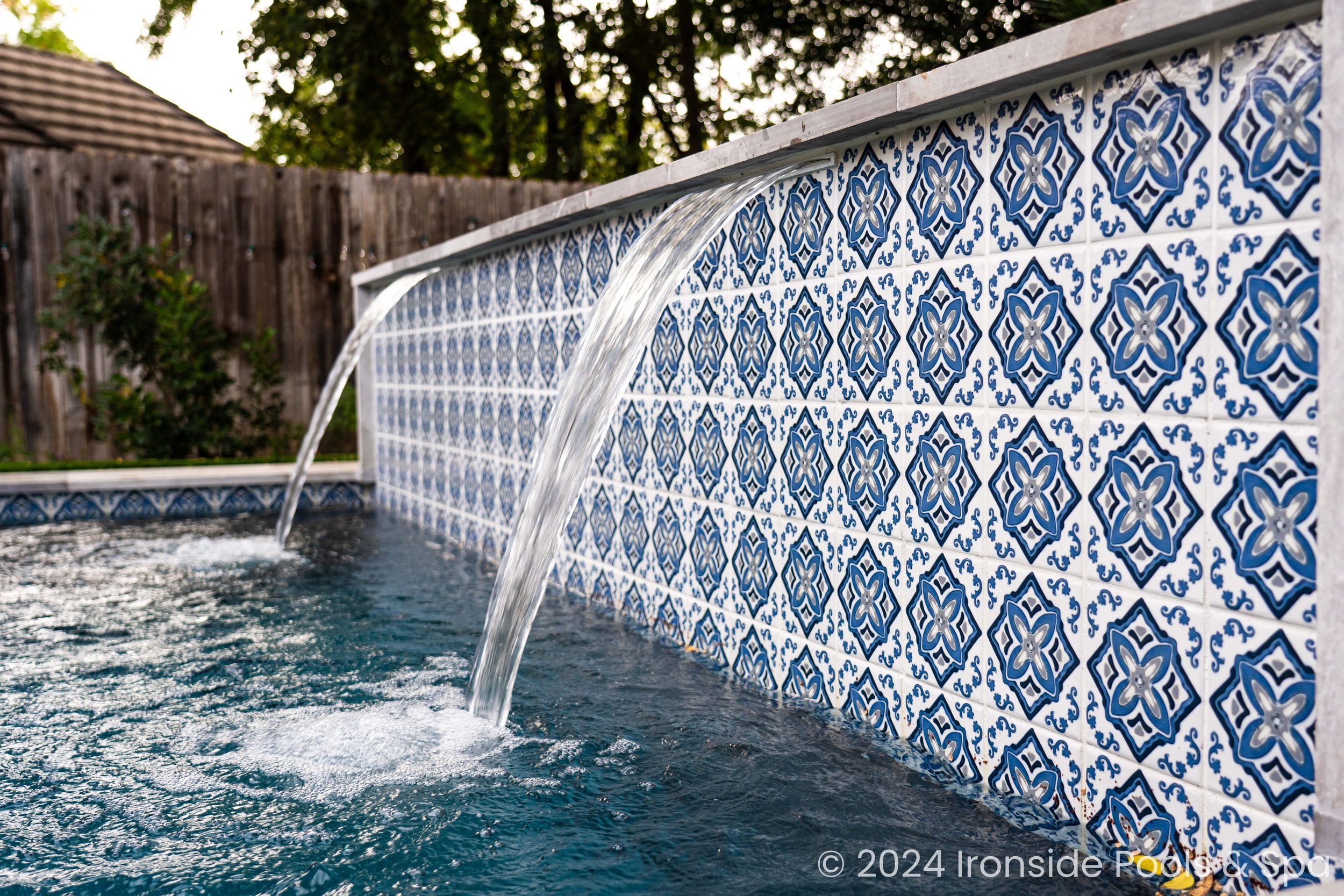Swimming pool with decorative blue and white tile wall and water spouts.