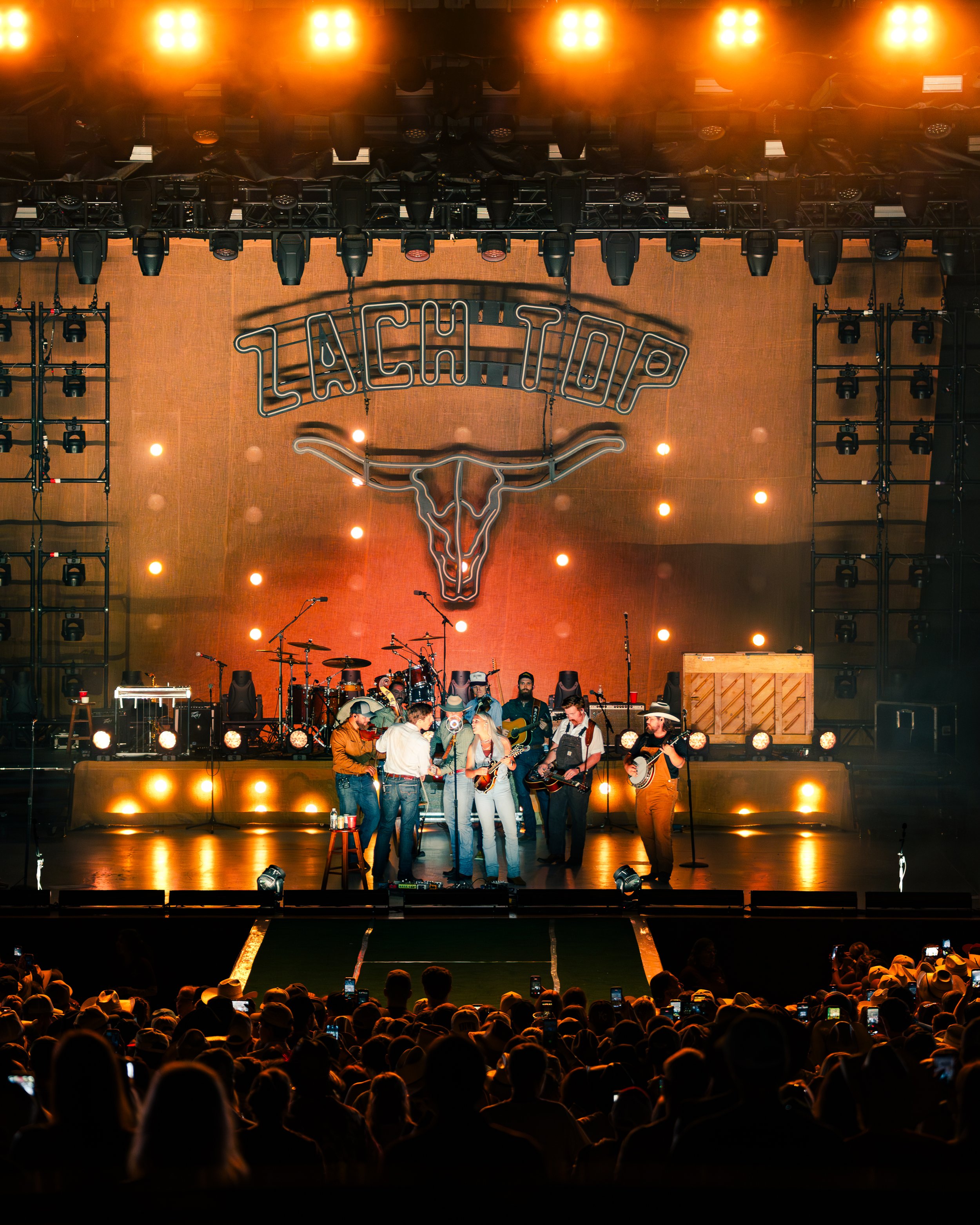 Musicians preparing on stage at a live concert with a large crowd in attendance.