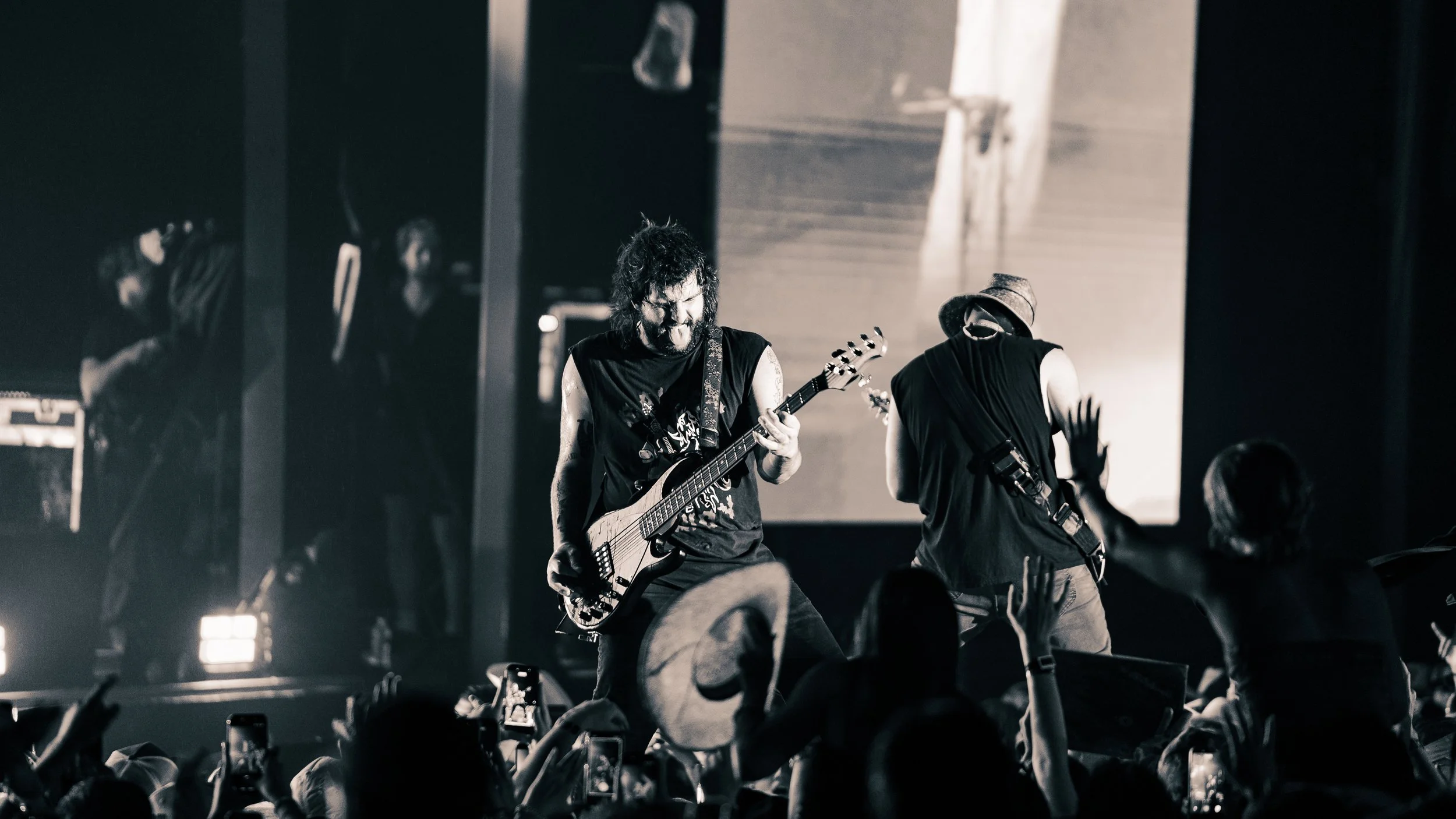 Black and white photo of a guitarist performing on stage with an audience in the foreground, some fans holding up phones.