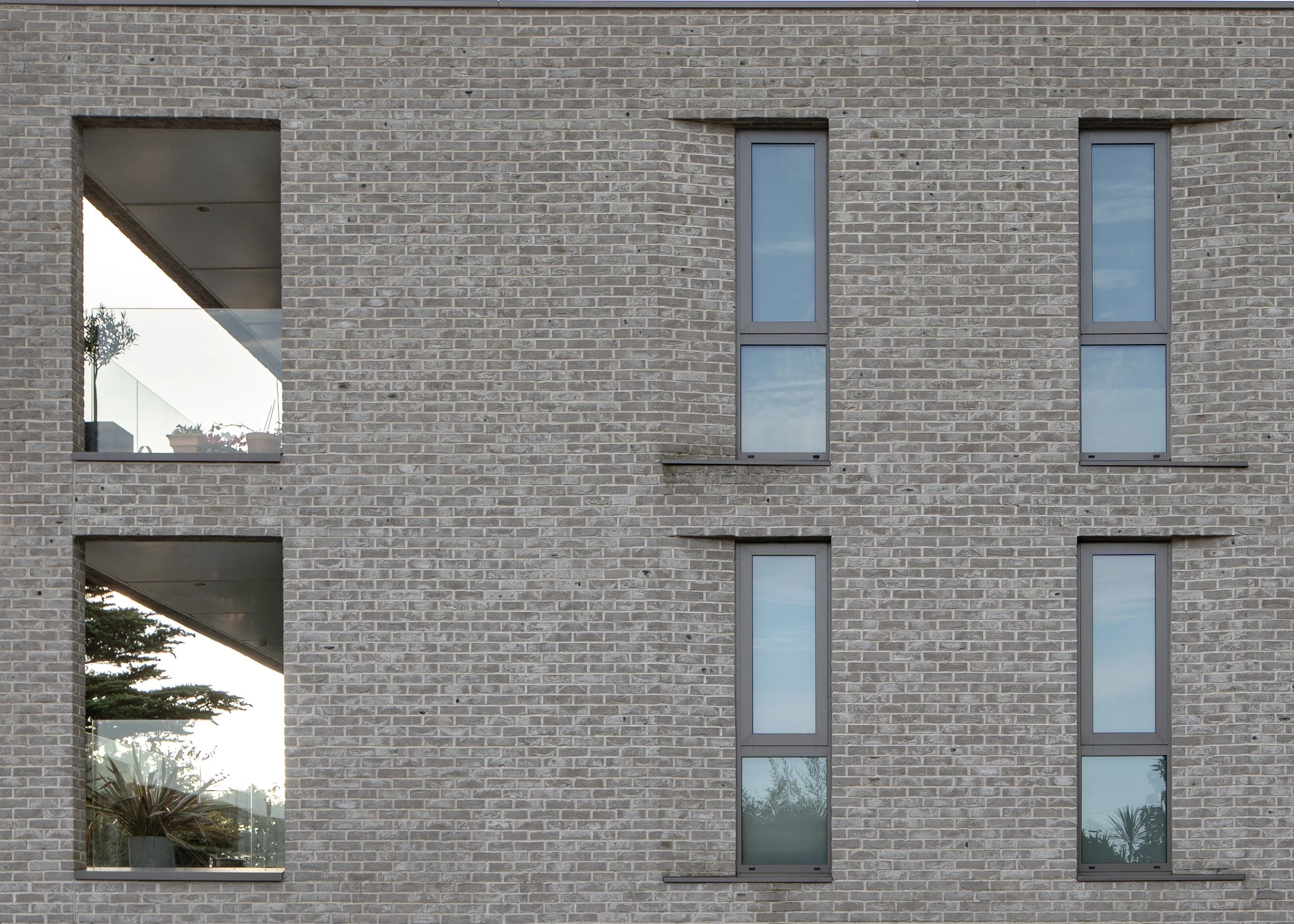Close-up of a modern building's brick exterior with three narrow, vertically oriented windows with reflective glass.