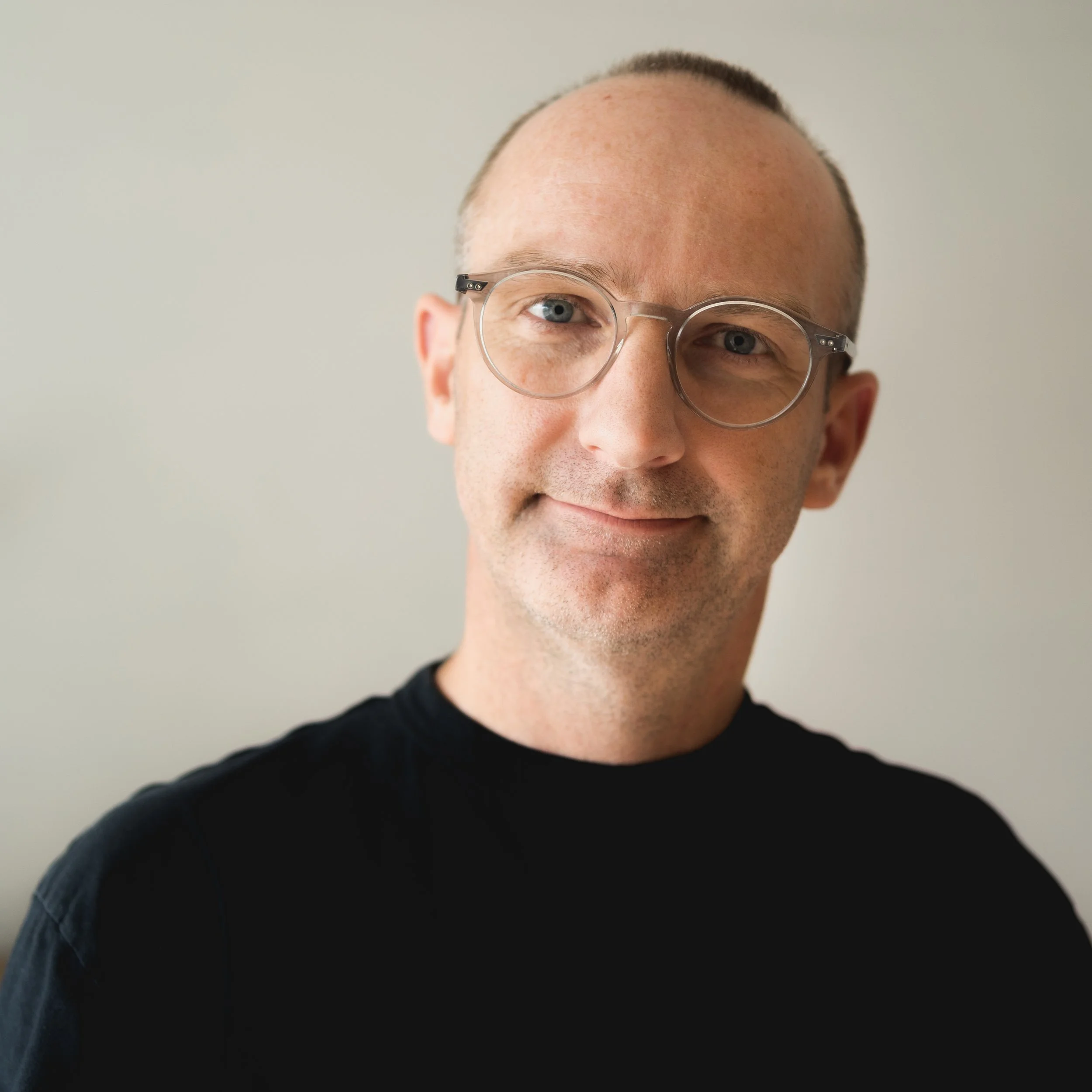 Phil Downes wearing glasses and a black shirt, smiling gently against a neutral background.