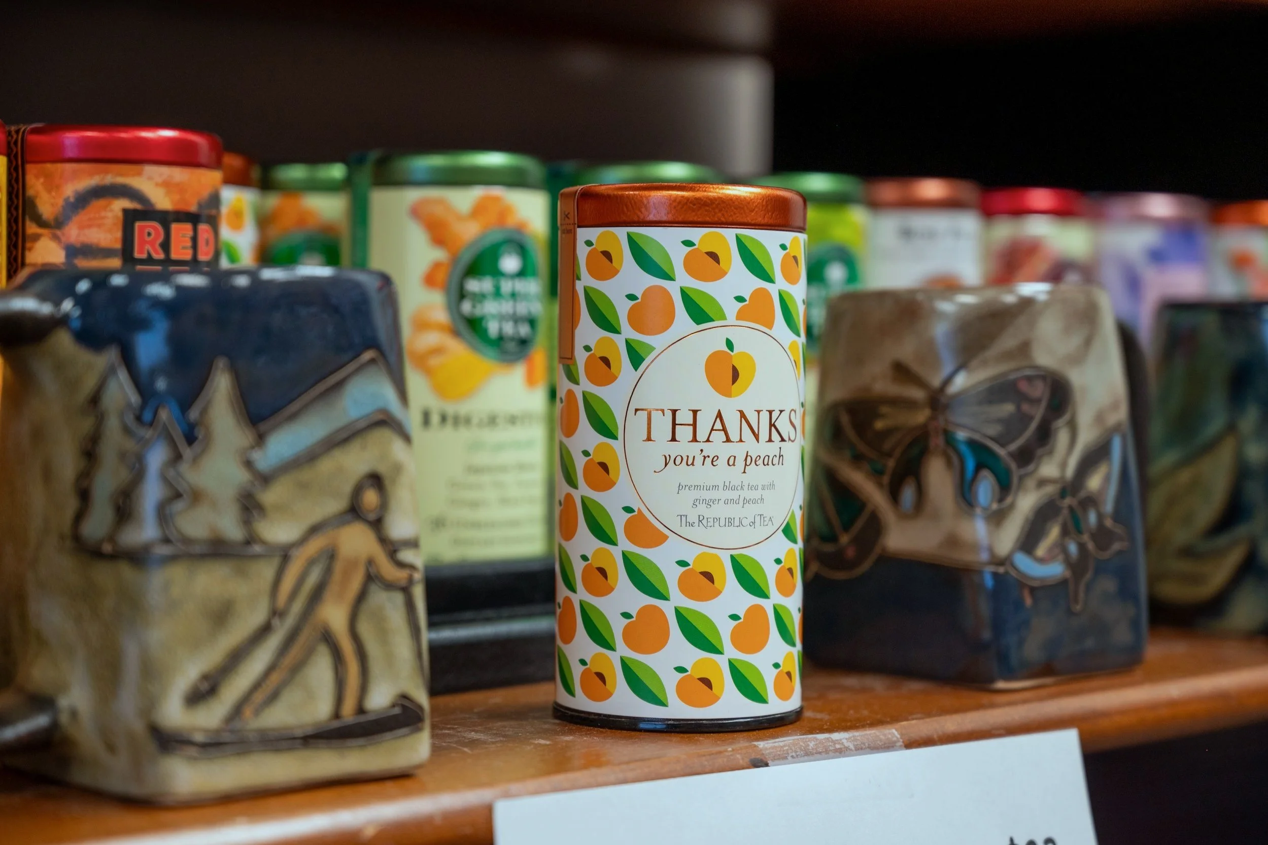 A can of peach-flavored tea with the label 'Thanks you're a peach' surrounded by colorful tea tins on a wooden shelf.