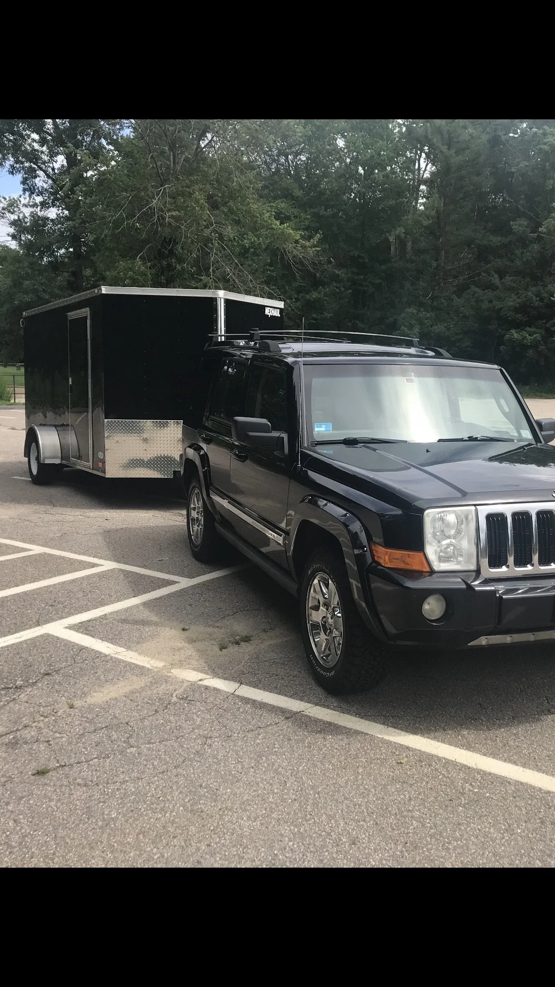 A black Jeep SUV with a trailer attached parked in an empty parking lot with trees in the background. RIFFT LLC
