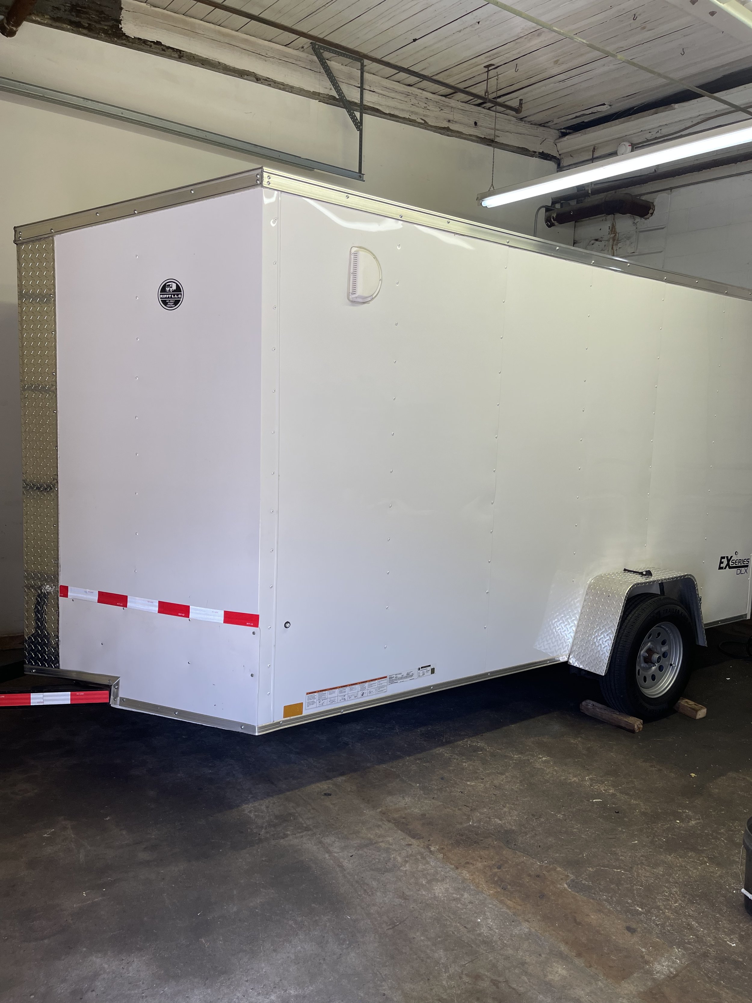White enclosed trailer with diamond plate accents parked inside a garage or warehouse showroom. RIFFT LLC