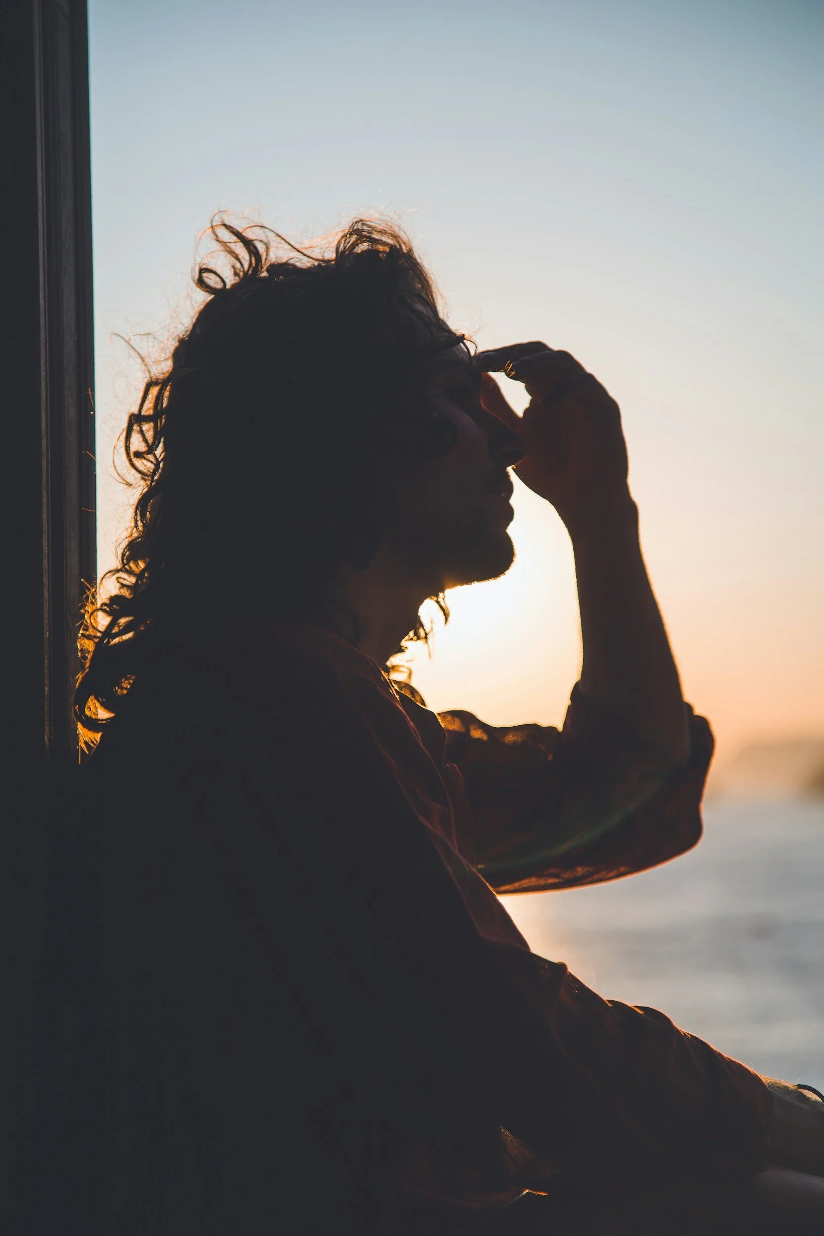 person with their hand on their forehead, a shadow with sunlight in the background