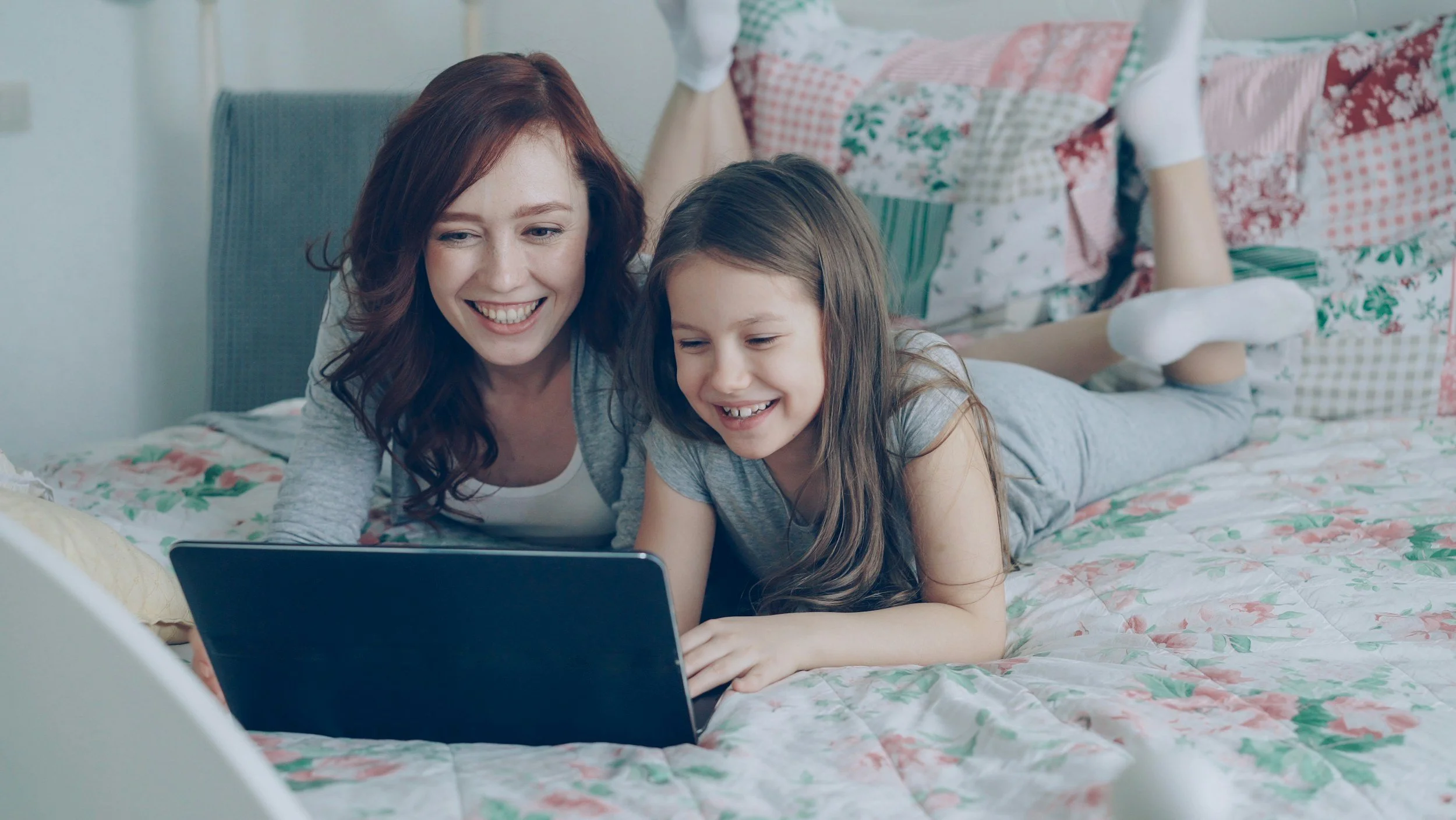 a mother and daughter staring at a screen smiling
