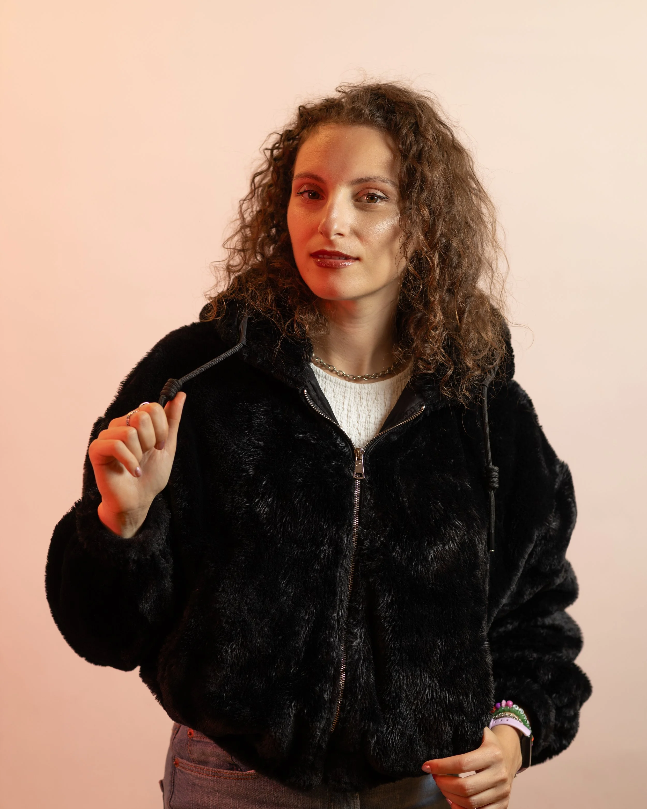 Female DJ with curly hair and a black furry jacket looks at the camera