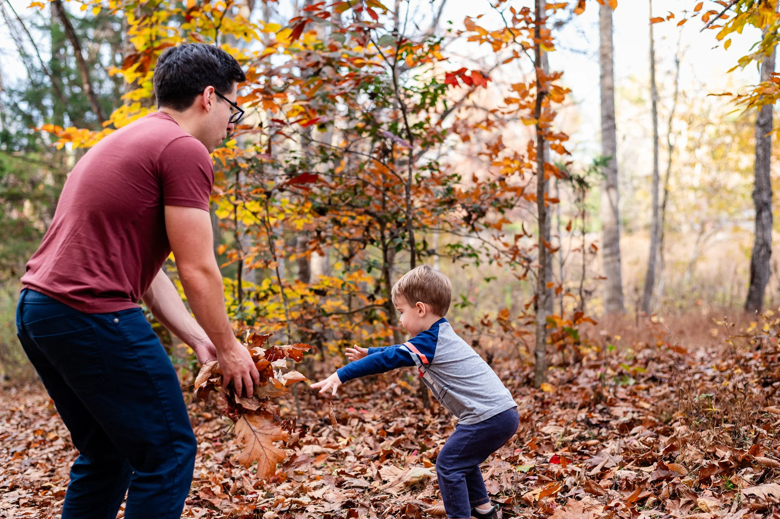 Dad playing in the leaves with toddler boy during fall family pictures at Ivy Creek Natural Area at sunset