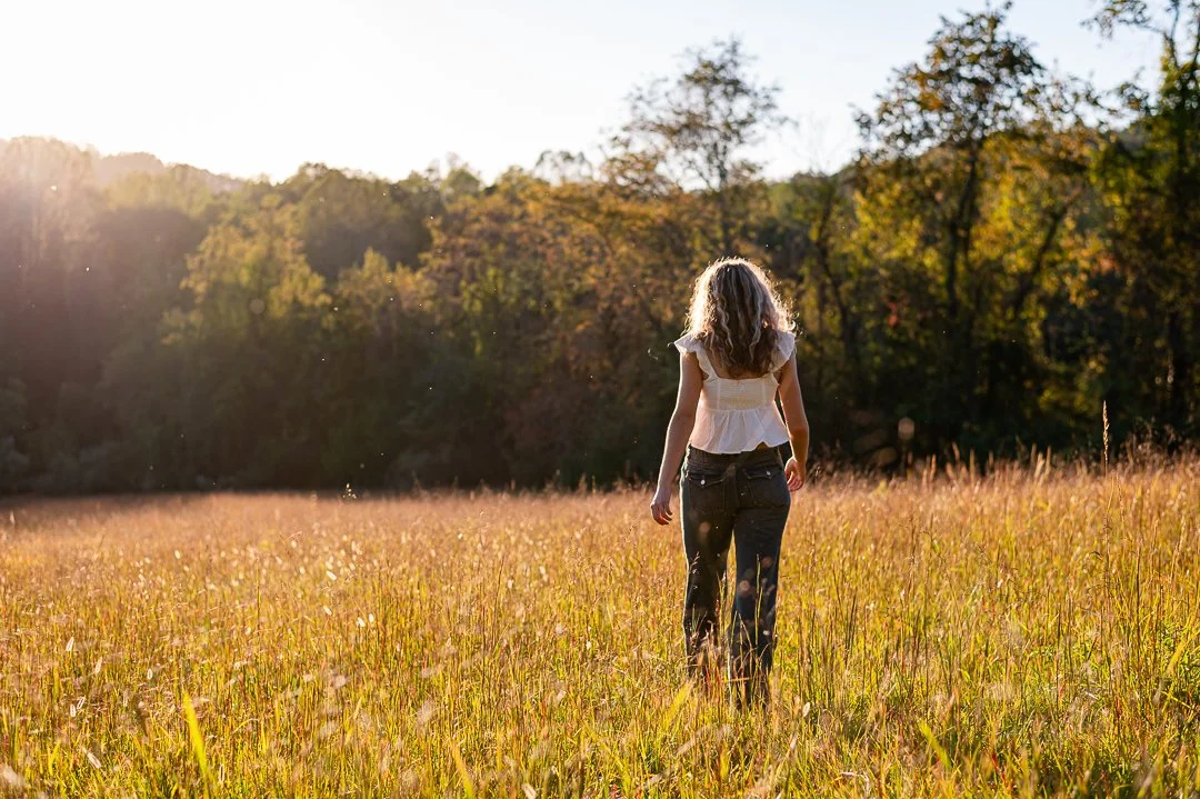 a senior girls walks through a meadow during a summer senior session held at golden hour at fox haven farms by Erin E Gallagher Photography